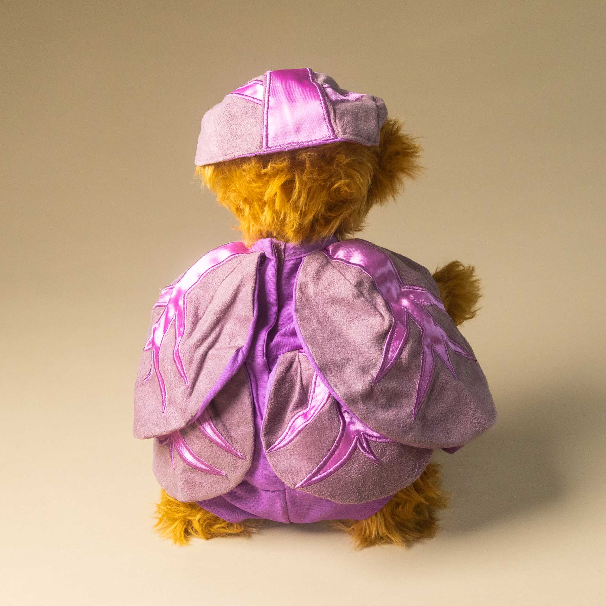 pickles-the-red-cabbage-bear wearing a purple outfit with a matching hat on a beige background