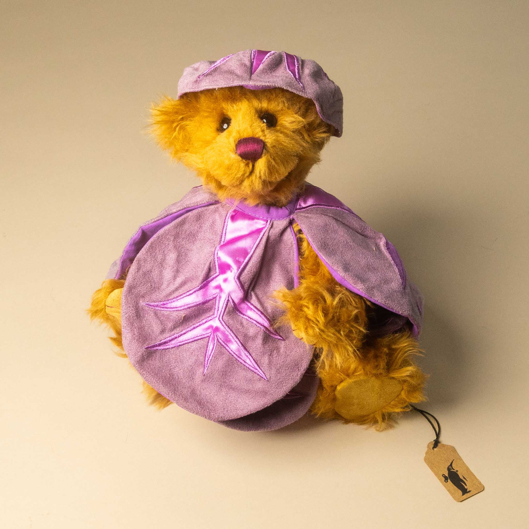 pickles-the-red-cabbage-bear in a purple outfit with a matching hat on a beige background