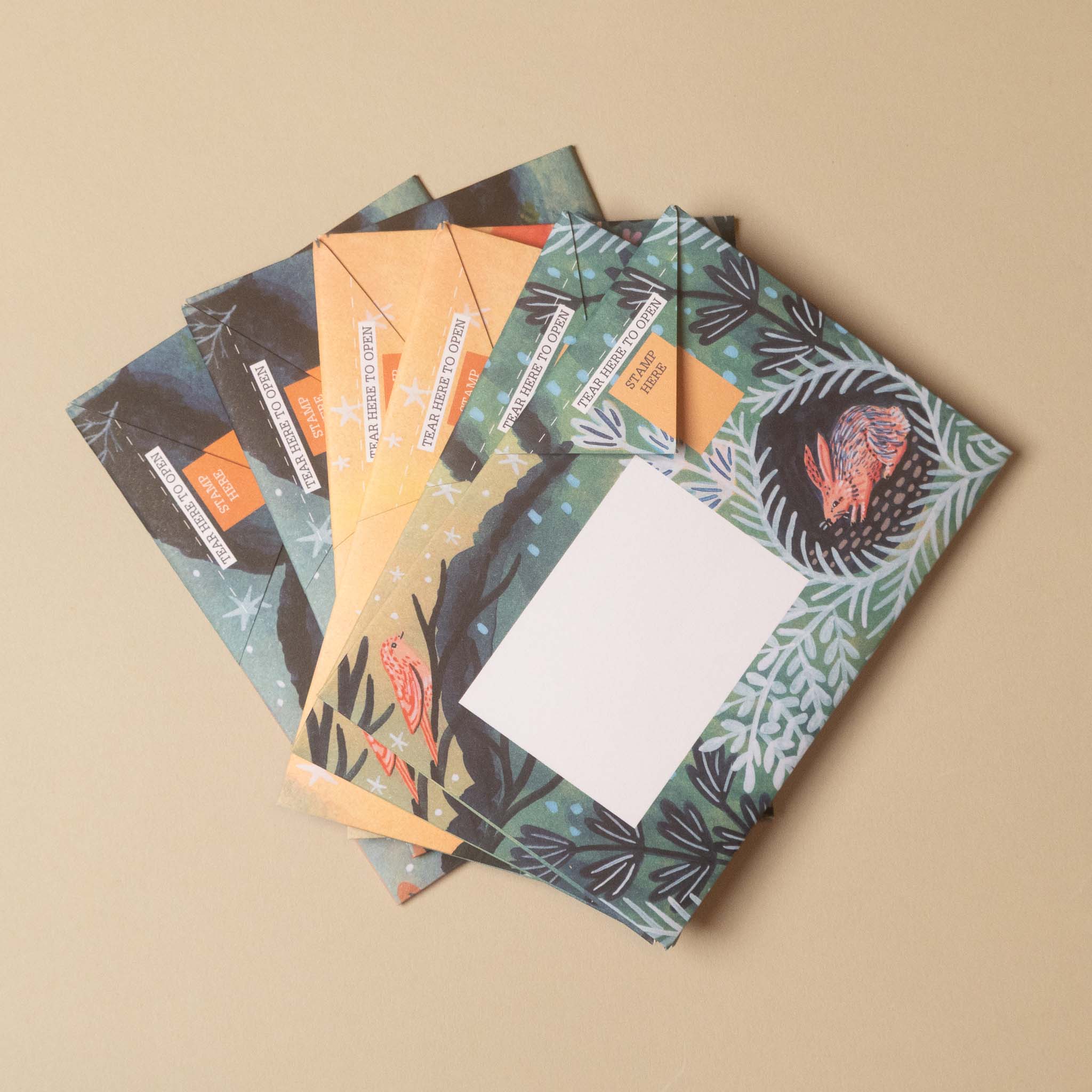 Four illustrated postcards fanned out on a warm beige background. The postcards feature whimsical, earthy illustrations including a sea turtle, a bird, a crab, and foliage in green, orange, yellow, and black.