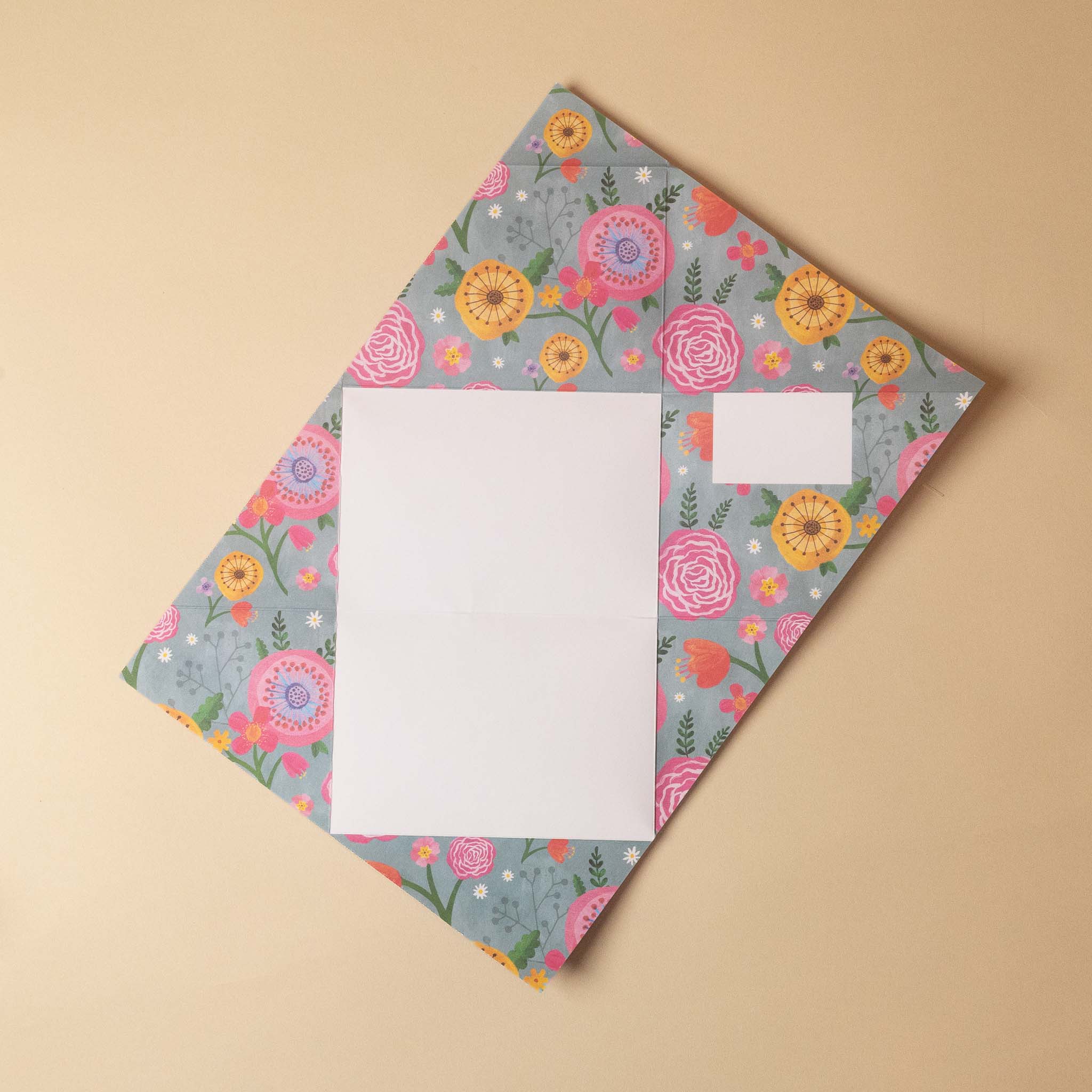 A floral-patterned envelope with a white insert card, photographed from above on a solid beige background.