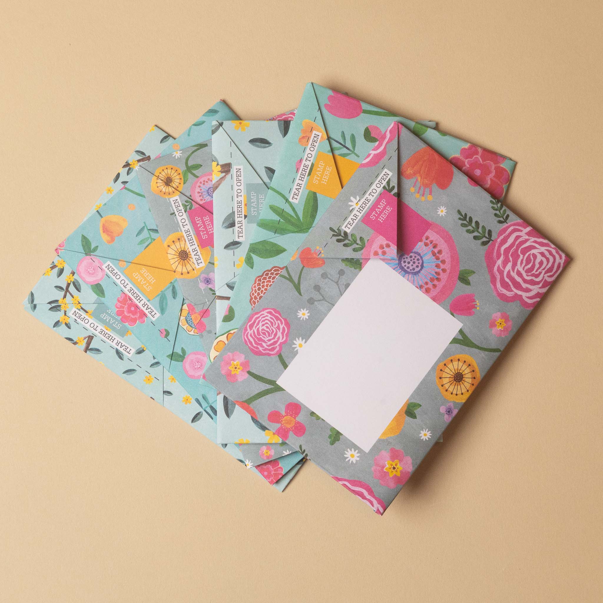Three floral patterned envelopes with blank white writing slots, arranged in a fan shape on a solid beige background.