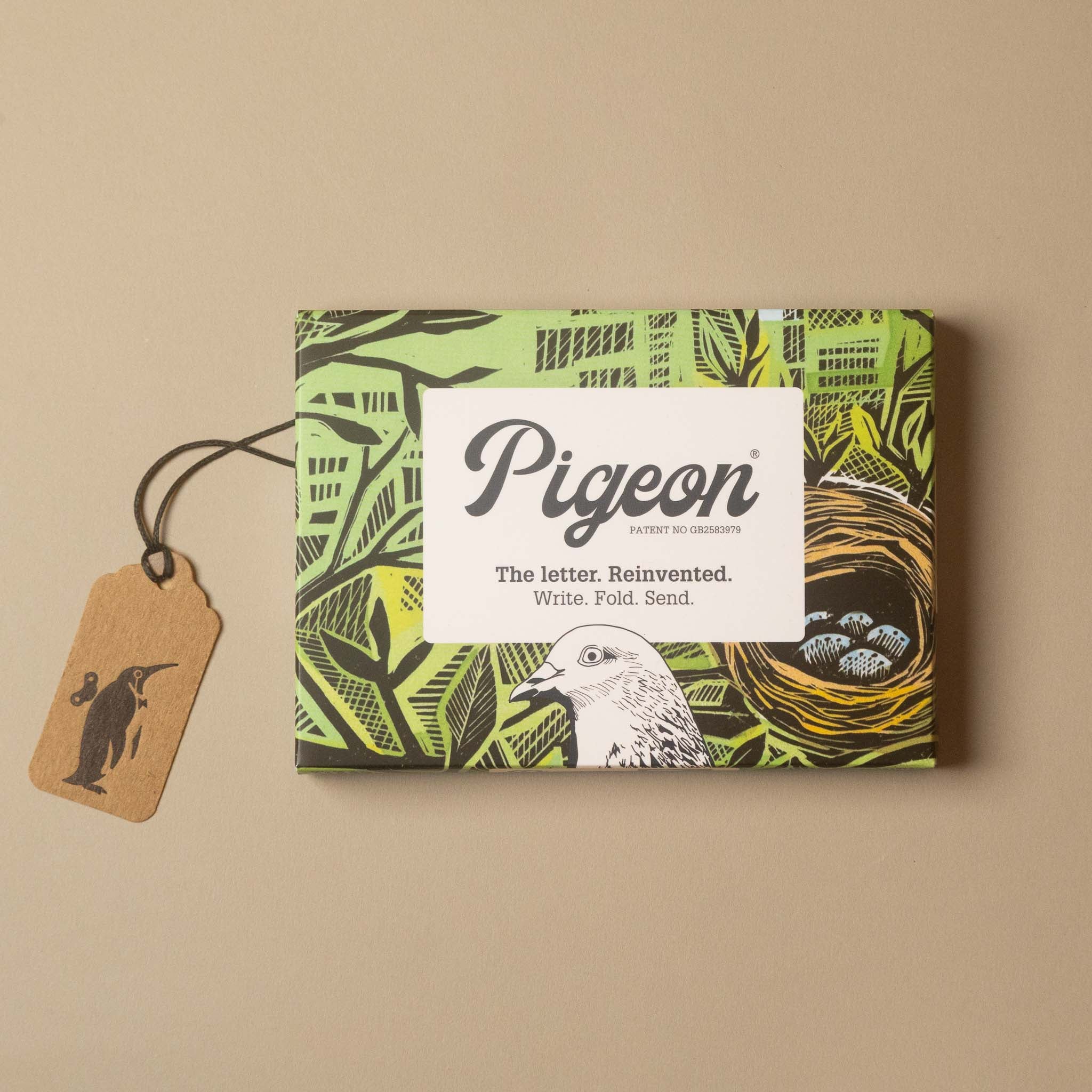 Pigeon stationery gift box with a green and black patterned design, featuring a white label with the brand name 'Pigeon' and a small kraft paper tag with a penguin silhouette, set against a solid beige background.