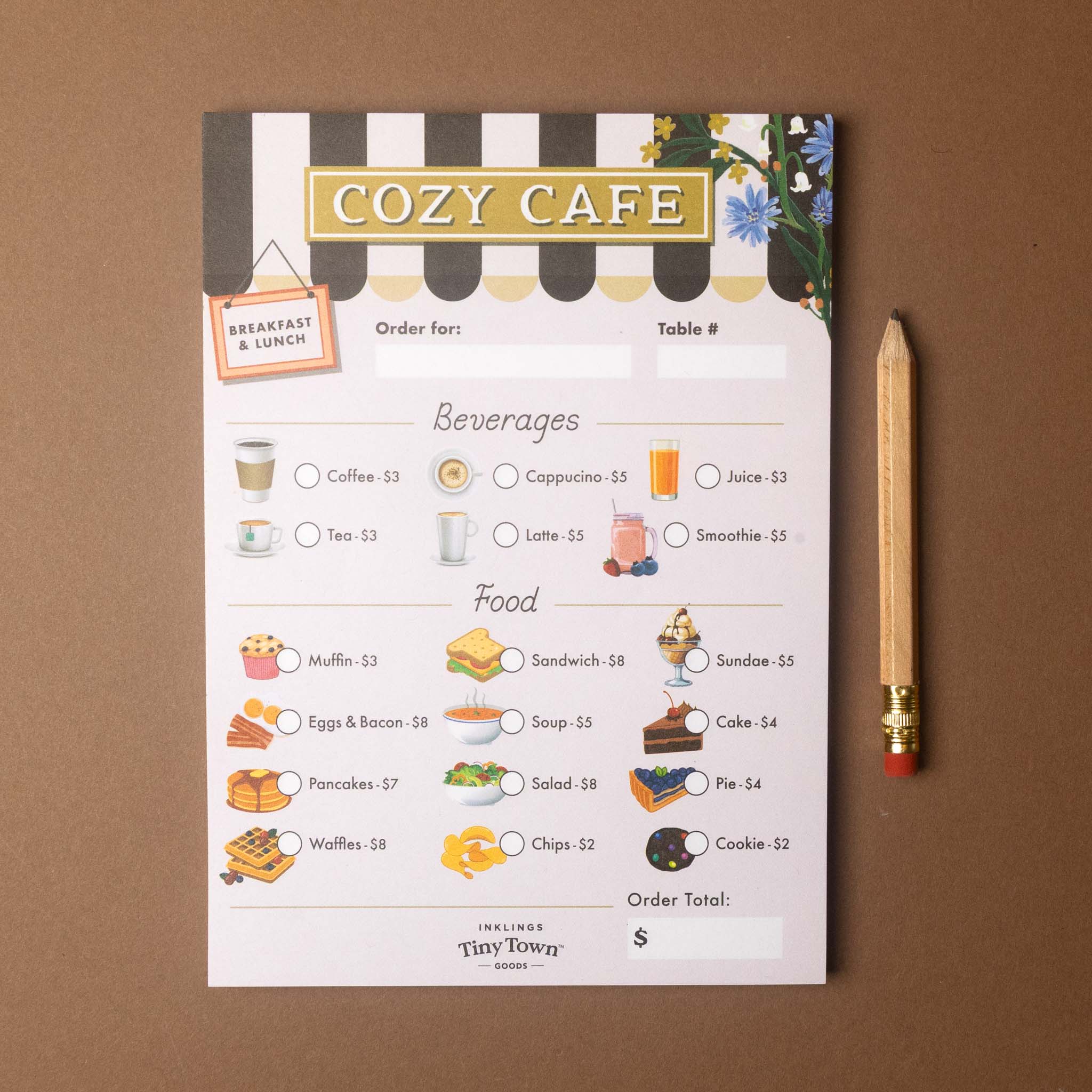 A flat-lay view of a 'Cozy Cafe' restaurant check card from 'Tiny Tower Studios' placed on a brown surface next to a wooden pencil. The check card features a black and white striped top header with a gold 'COZY CAFE' banner, and sections for ordering beverages and food with price circles.