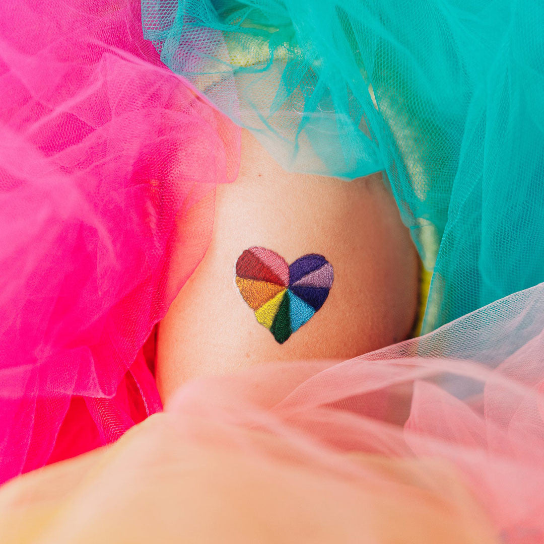 Colorful heart tattoo on a person's arm with colorful tulle in the background