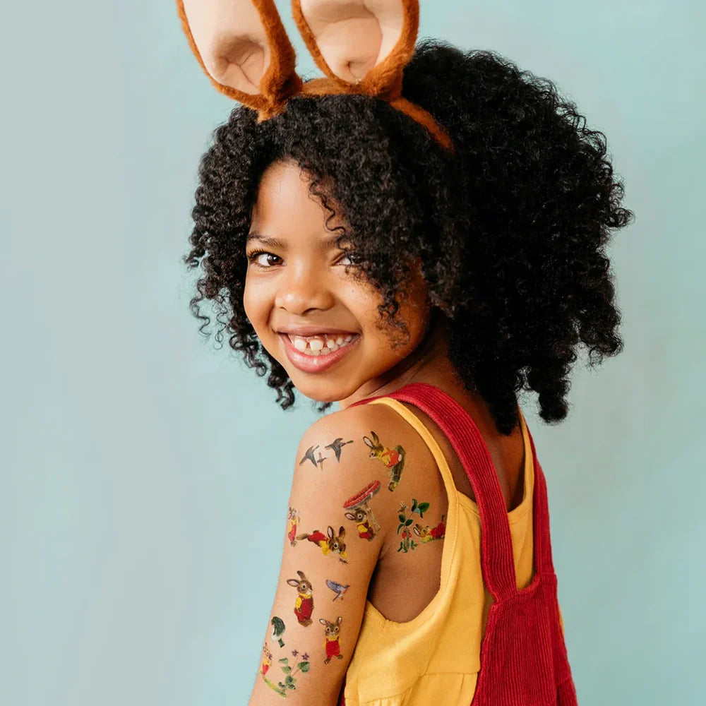 Child wearing bunny ears with richard-scarrys-bunny-temporary-tattoo-sheet on a light blue background