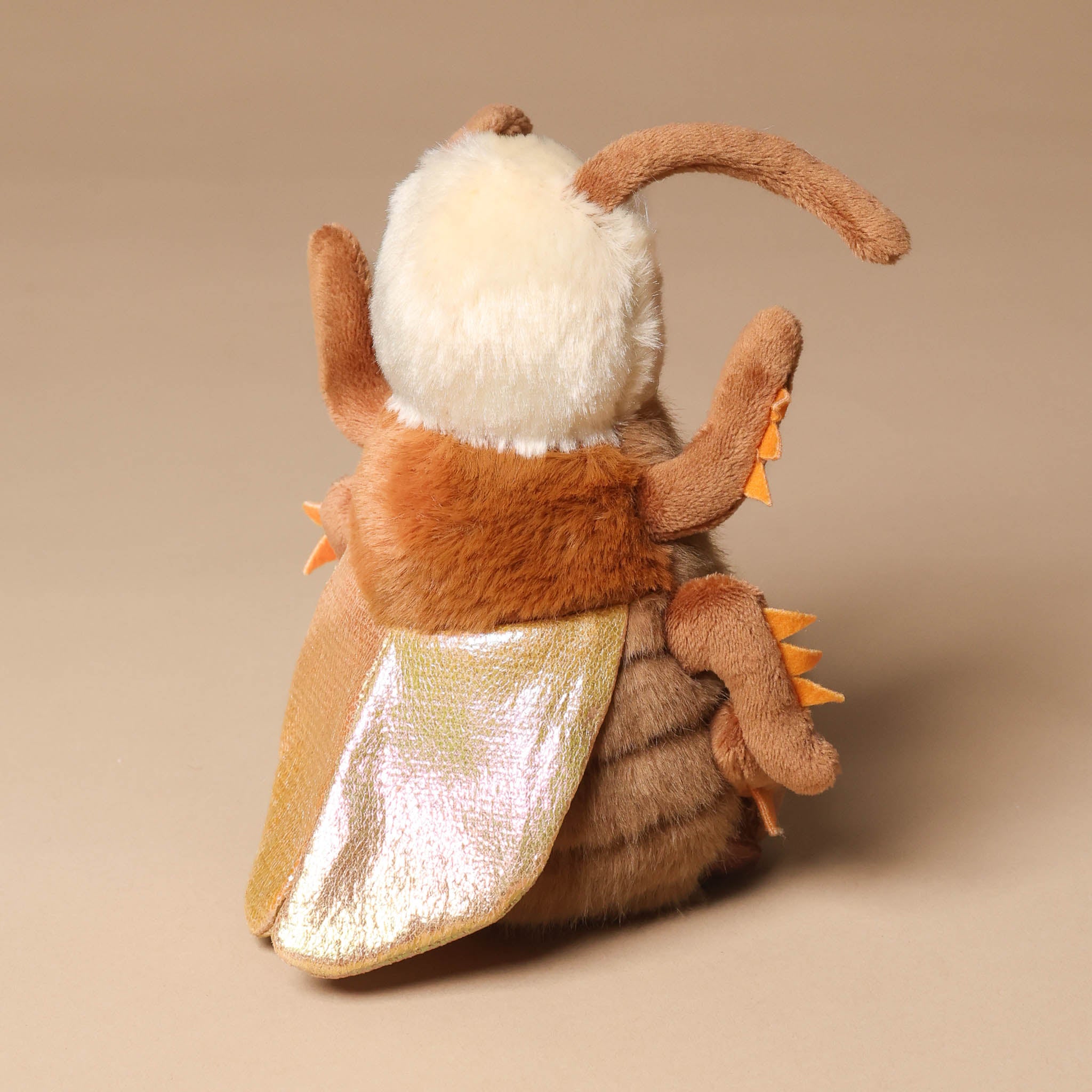 Plush toy rrocco-the-cockroach with brown fur and white face on a beige background