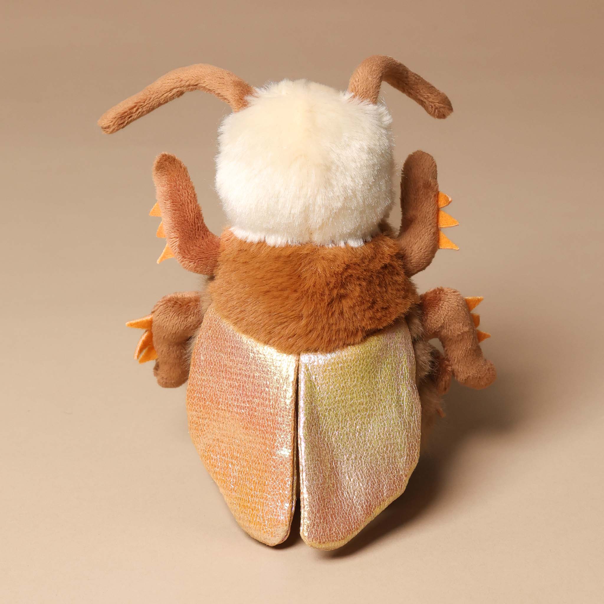 Plush toy rrocco-the-cockroach with brown fur and white face on a beige background