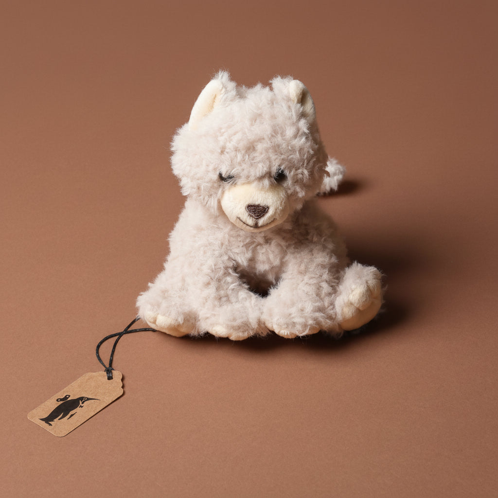 Plush romy-the-cat-petite toy with a tag on a brown background