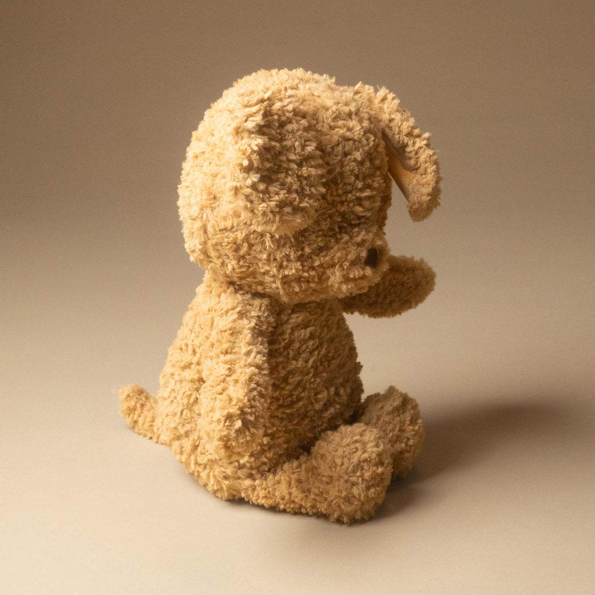rufus-the-dog in a textured, curly tan fabric, shown from a side-back angle on a warm beige studio background.