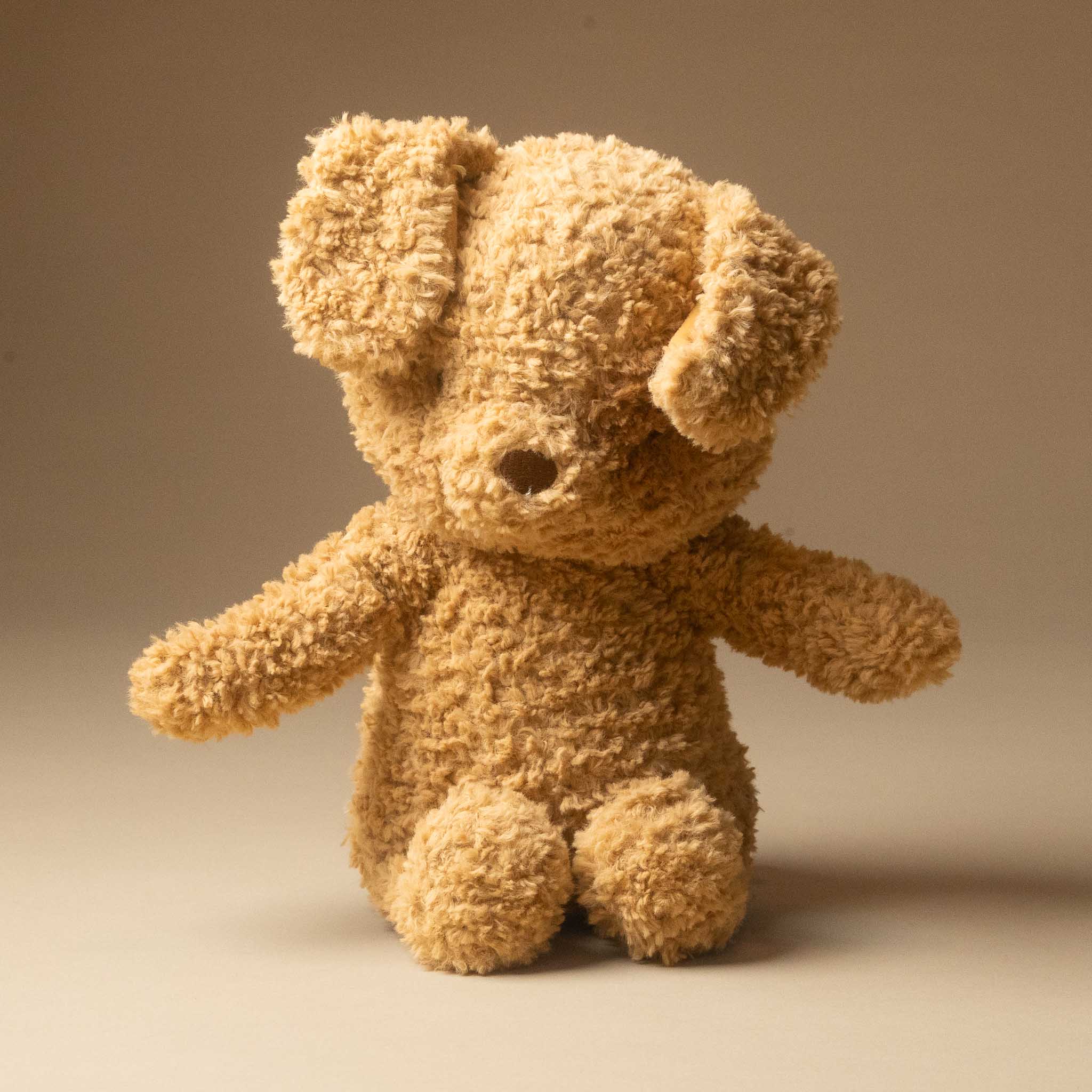 rufus-the-dog made from curly, bouclé-like fabric in a warm tan or light brown color, photographed against a plain beige studio background.