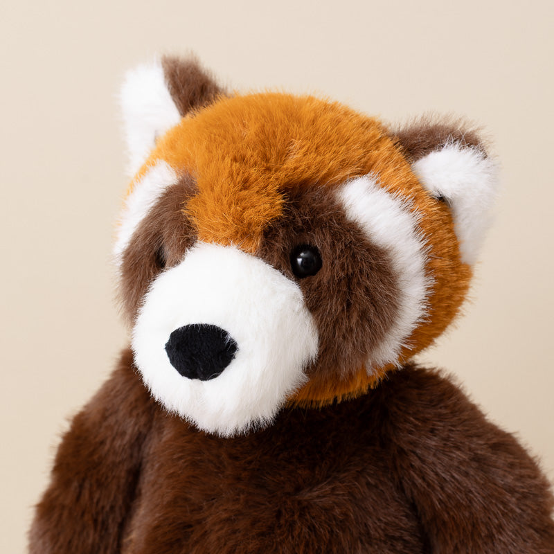 A close-up of a plush red panda toy against a solid beige background.