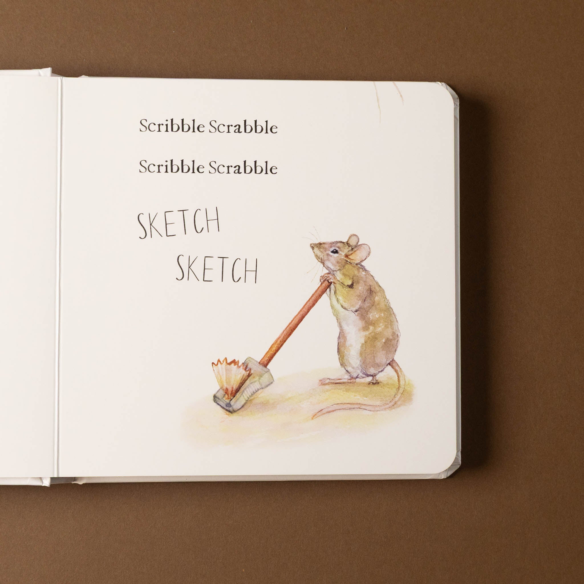 Open scribble-scrabble-a-first-words-and-shapes-board-book with a mouse illustration holding a brush and text on a brown background
