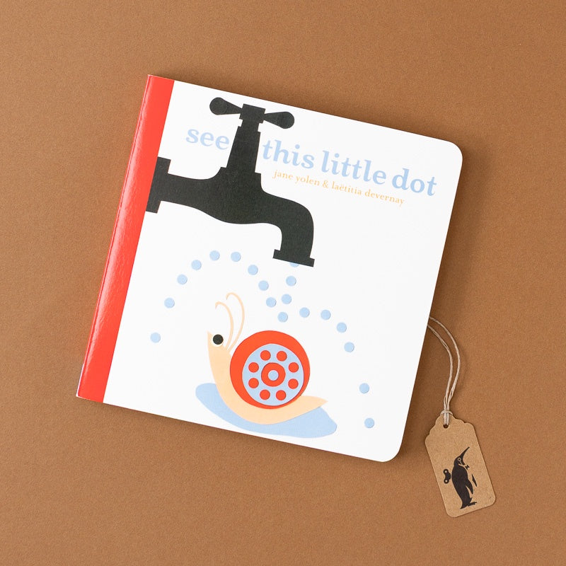A children's board book titled 'see this little dot' by Jane Yolen & Laura Dewdney, featuring a white cover with a red spine, a black faucet illustration, and a snail with a red and orange spotted shell. A small paper tag hangs from the right side, placed on a brown background.