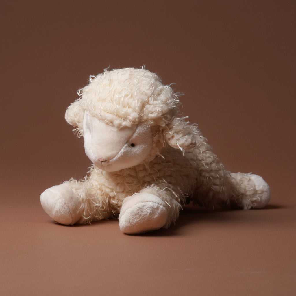 White fluffy toy shep-the-sheep-medium with a tag on a brown background