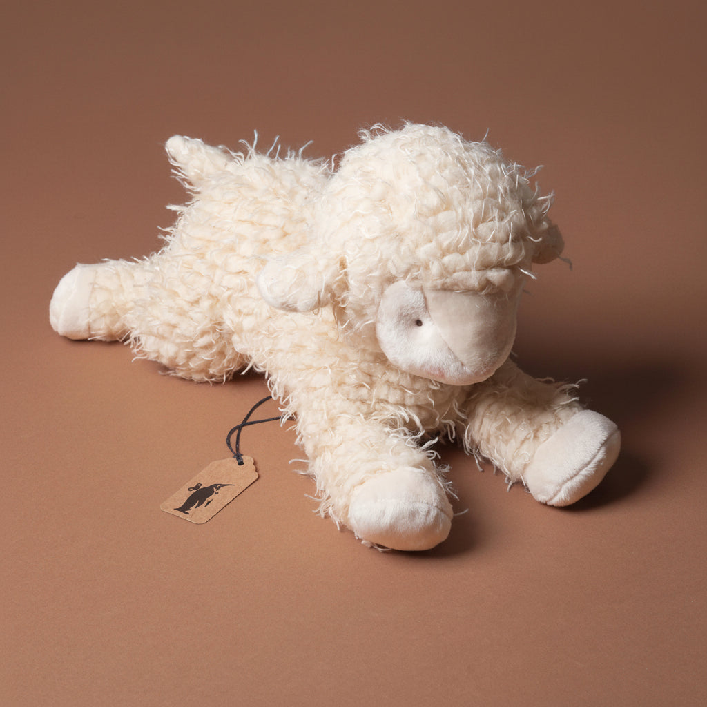 White fluffy toy shep-the-sheep-medium with a tag on a brown background