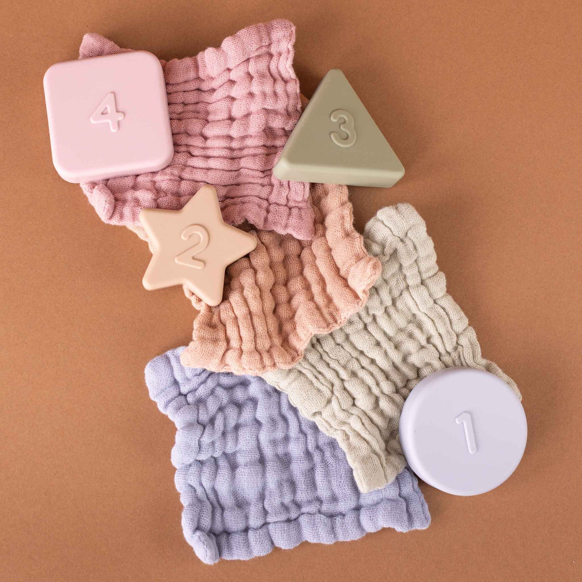 Four textured baby wipes in soft pastel colors arranged on a warm brown background, with matching numbered wipes blocks (1, 2, 3, 4) placed on top.