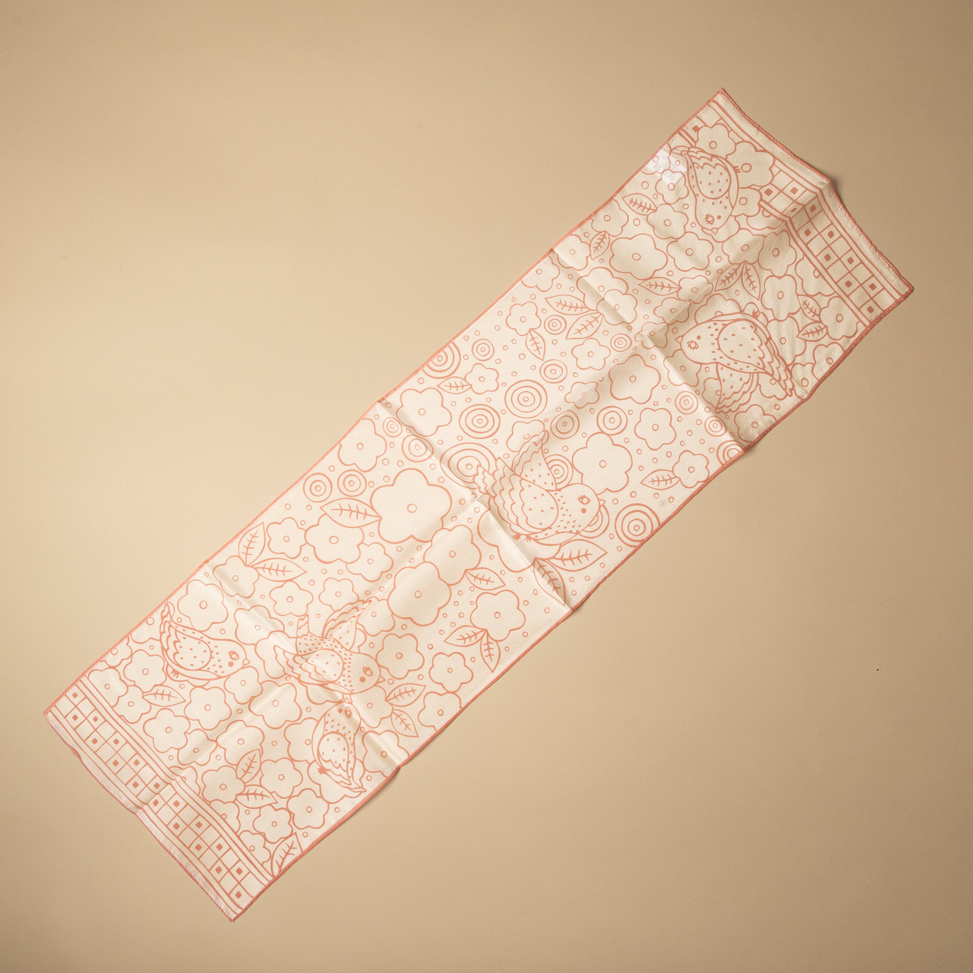 A long rectangular scarf or bandana laid flat on a warm beige background. The fabric is off-white with a delicate coral-pink floral and geometric pattern.
