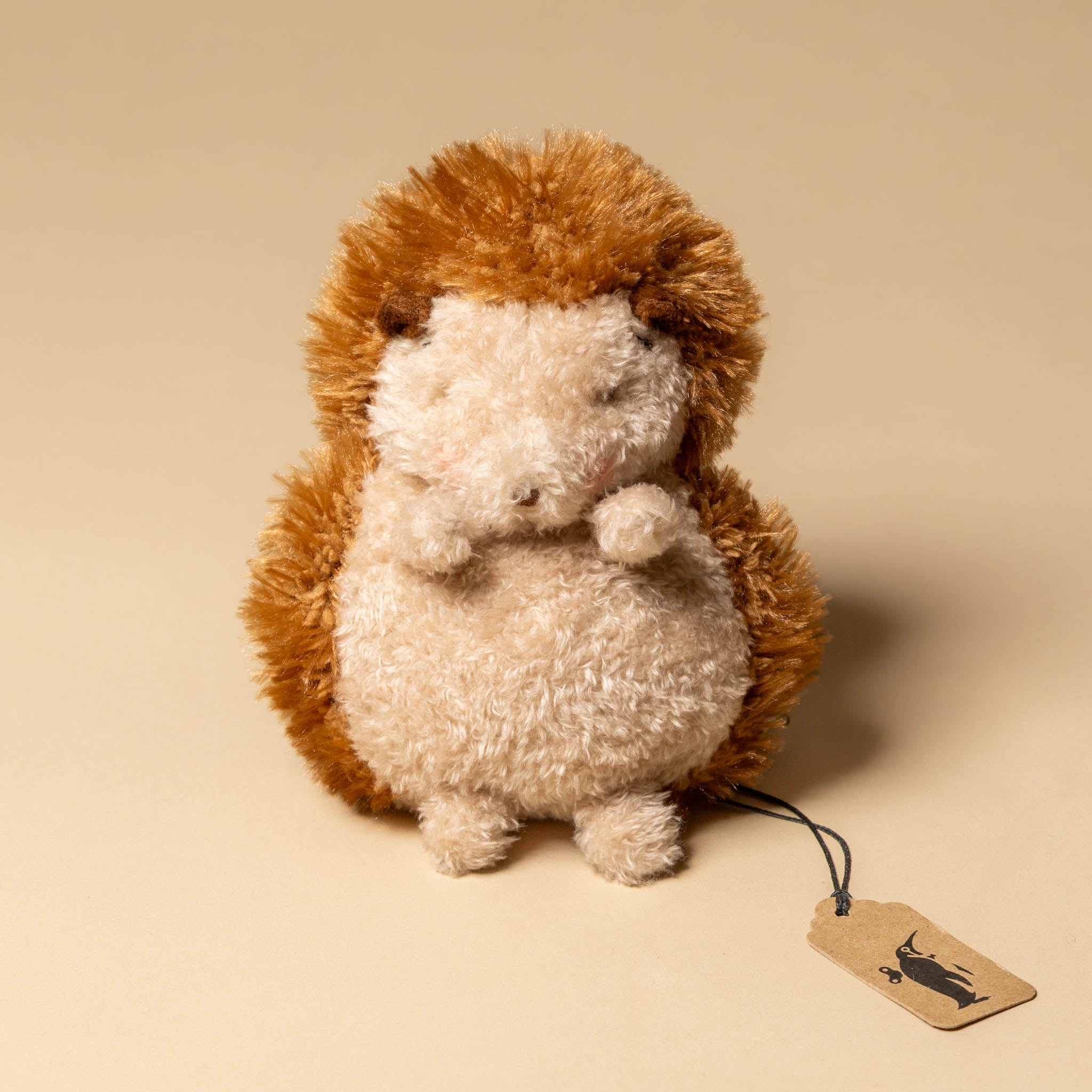 smidgen-the-hedgehog Plush hedgehog toy with a tag on a beige background