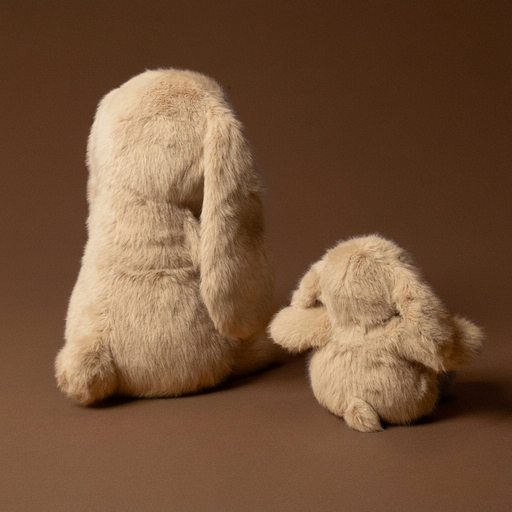 Two beige plush bunnies on a brown background
