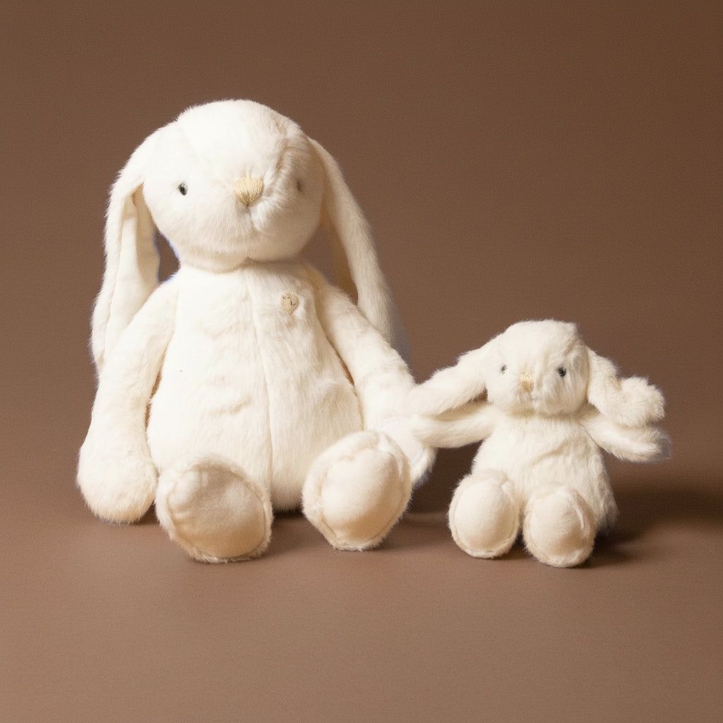 Two cream-colored plush bunnies on a brown background