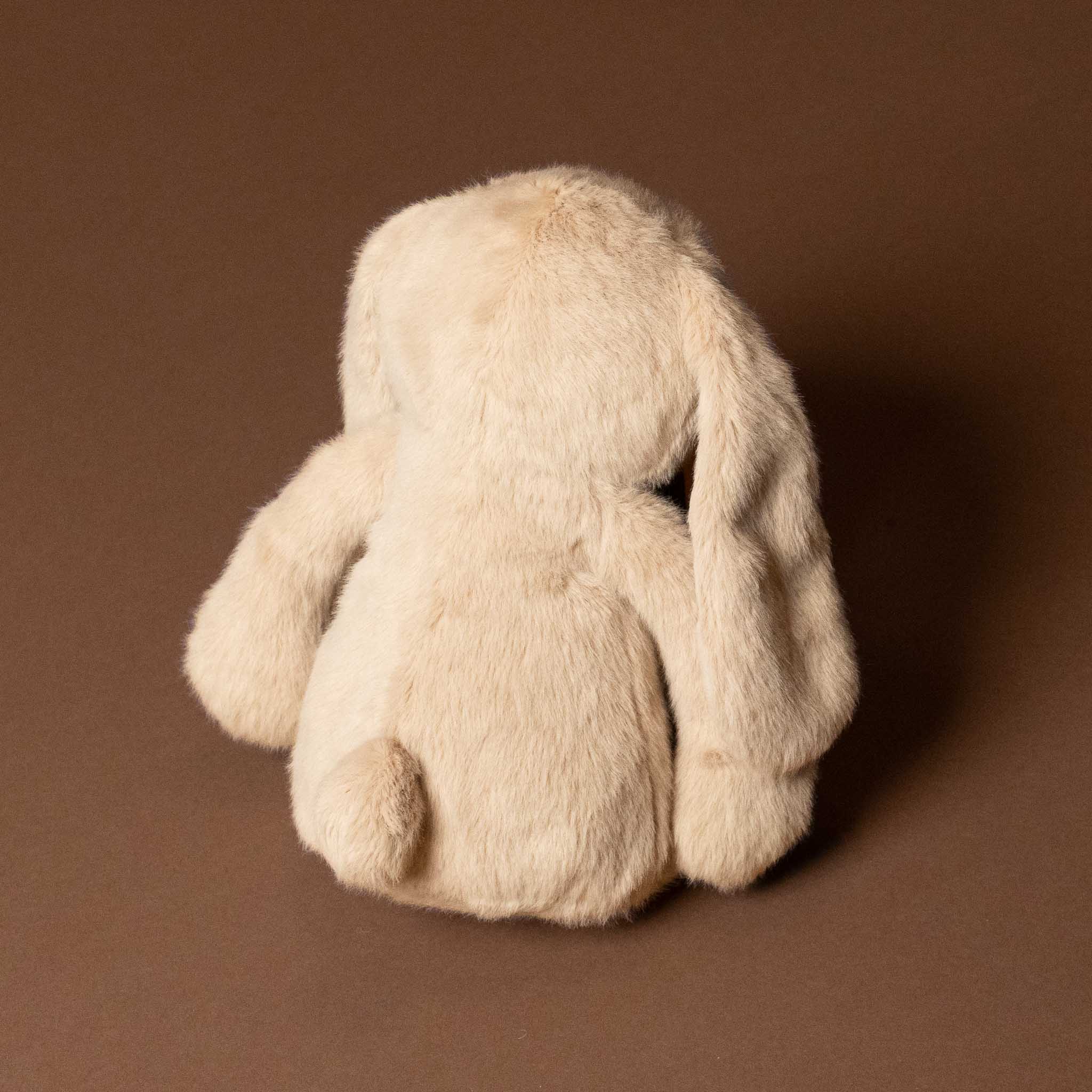 Beige plush snuggle-bunny-caramel toy on a brown background
