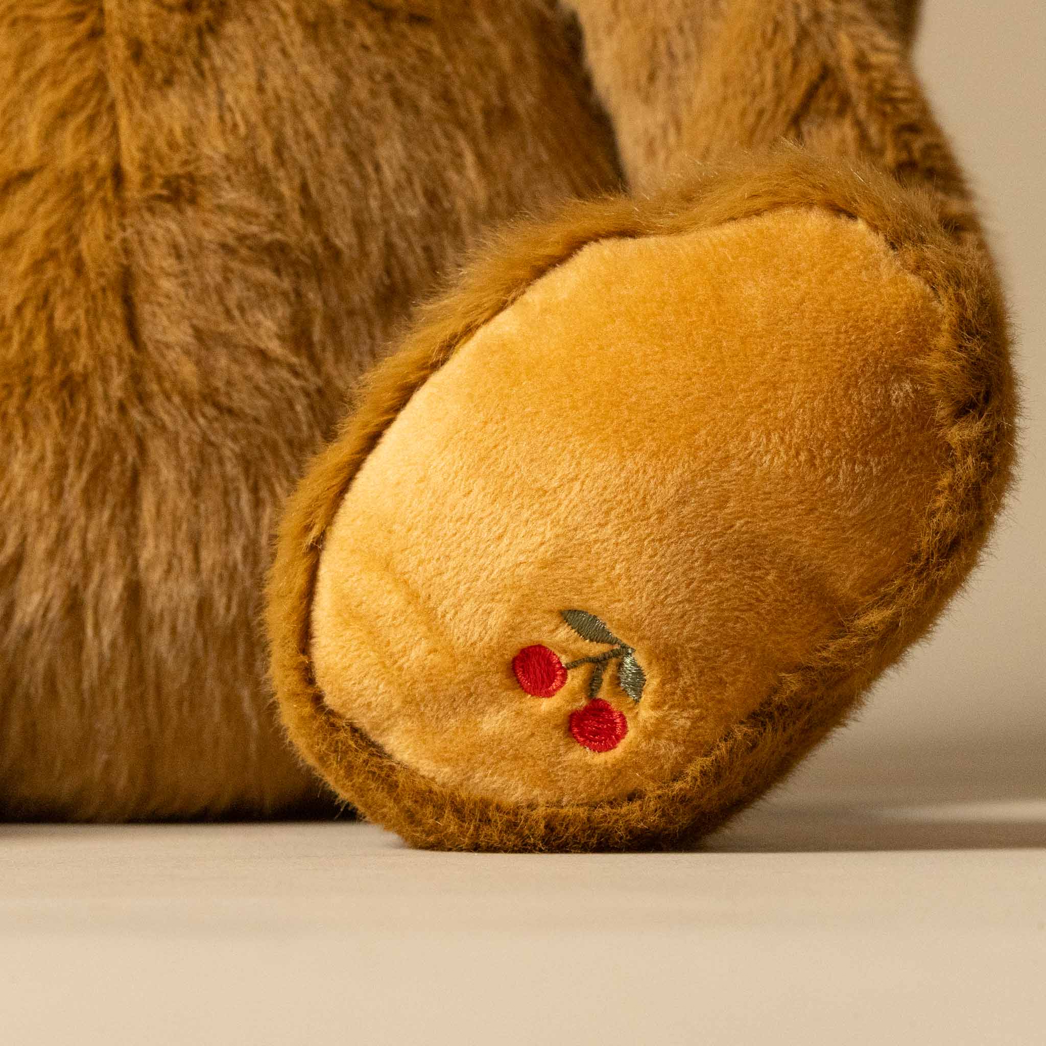 Close-up of a snuggle-bunny-toffee's paw with embroidered cherries on a neutral background