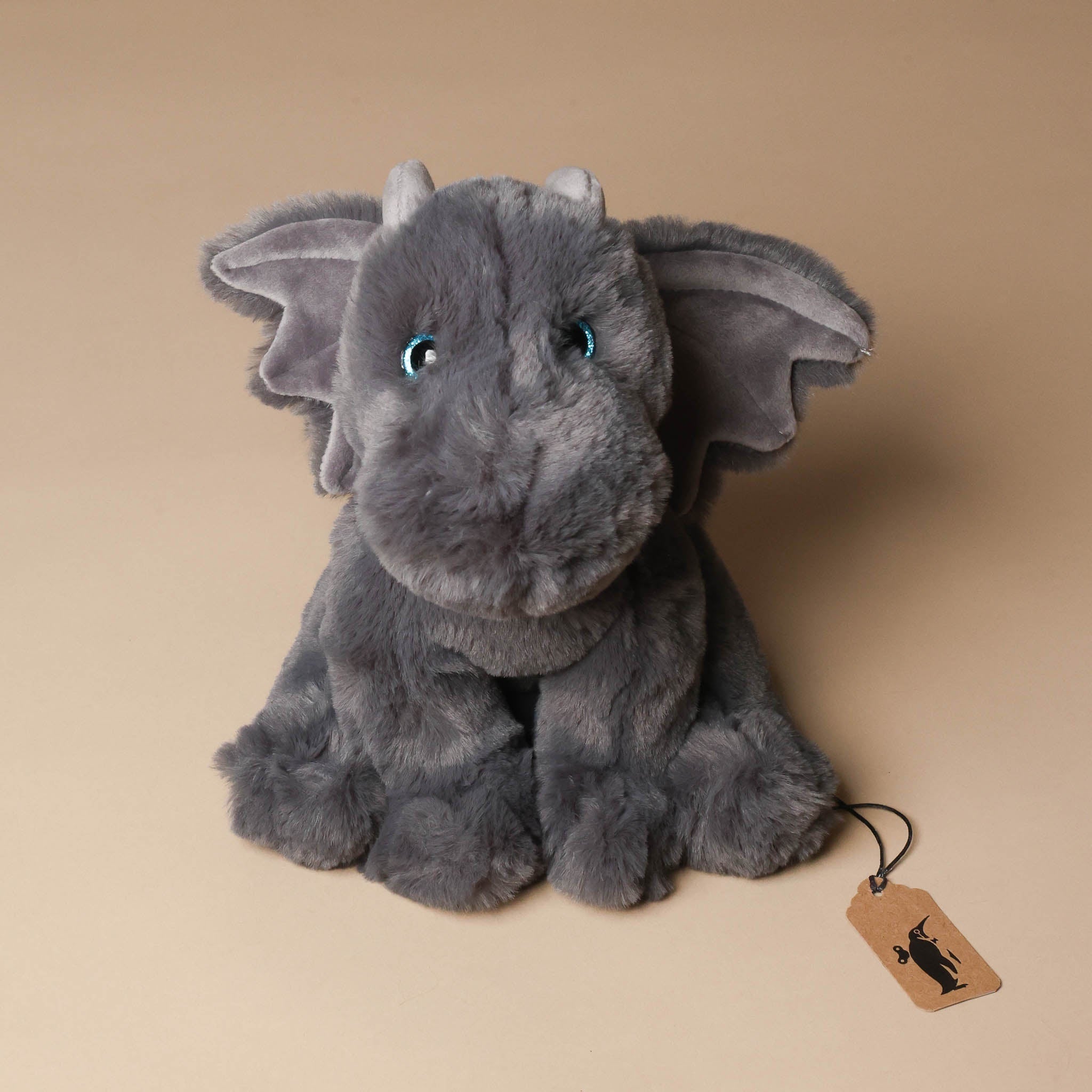 Gray plush dsootie-the-dragon toy with a tag on a beige background