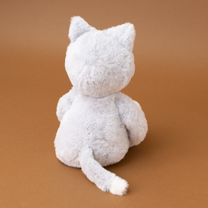 A light gray plush cat toy shown from the back, sitting on a smooth brown studio background.