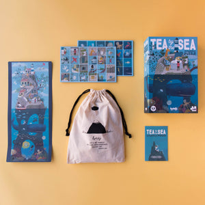 Tea-by-the-Sea-100-piece-Interactive-Puzzle-box-with-a-whale-under-an-island-with-coral-beneath-the-water-and-a-tea-party-above-and-carrying-bag