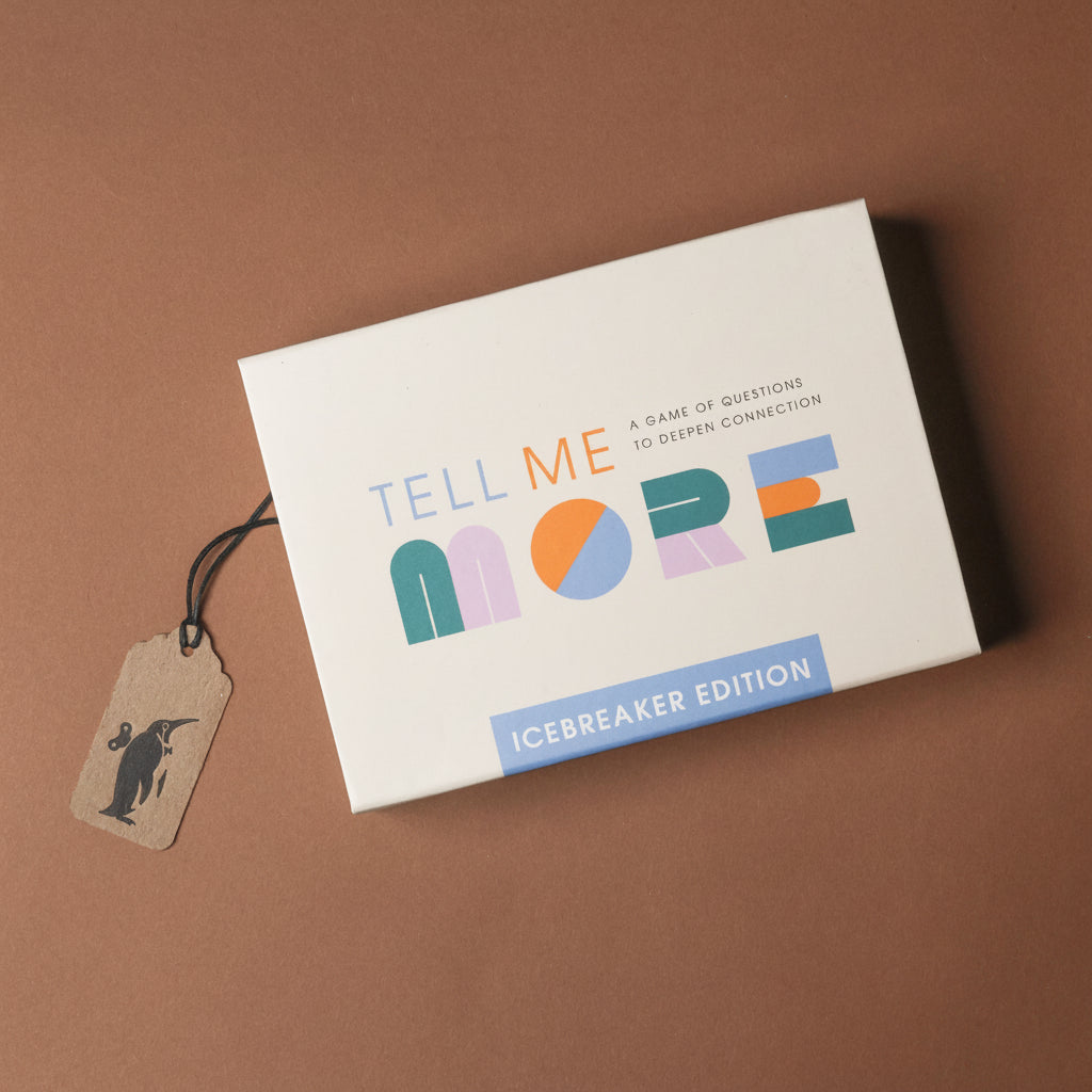 Card game box titled 'Tell Me More' with a tag on a brown background