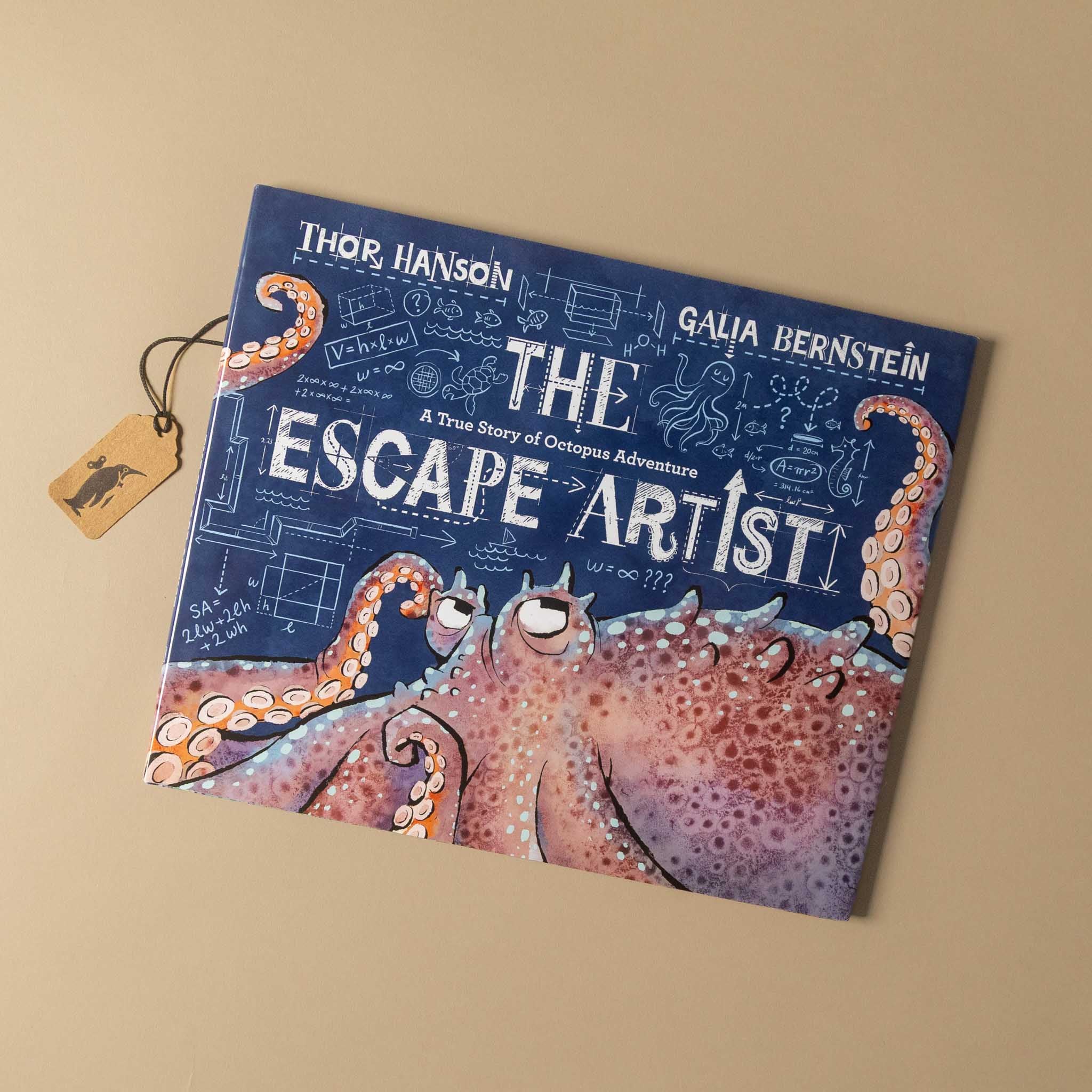The Escape Artist book by Thor Hanson and Galia Bernstein, featuring a dark blue cover with white title text and an illustration of a pink and orange octopus, photographed on a beige background with a small hanging tag.