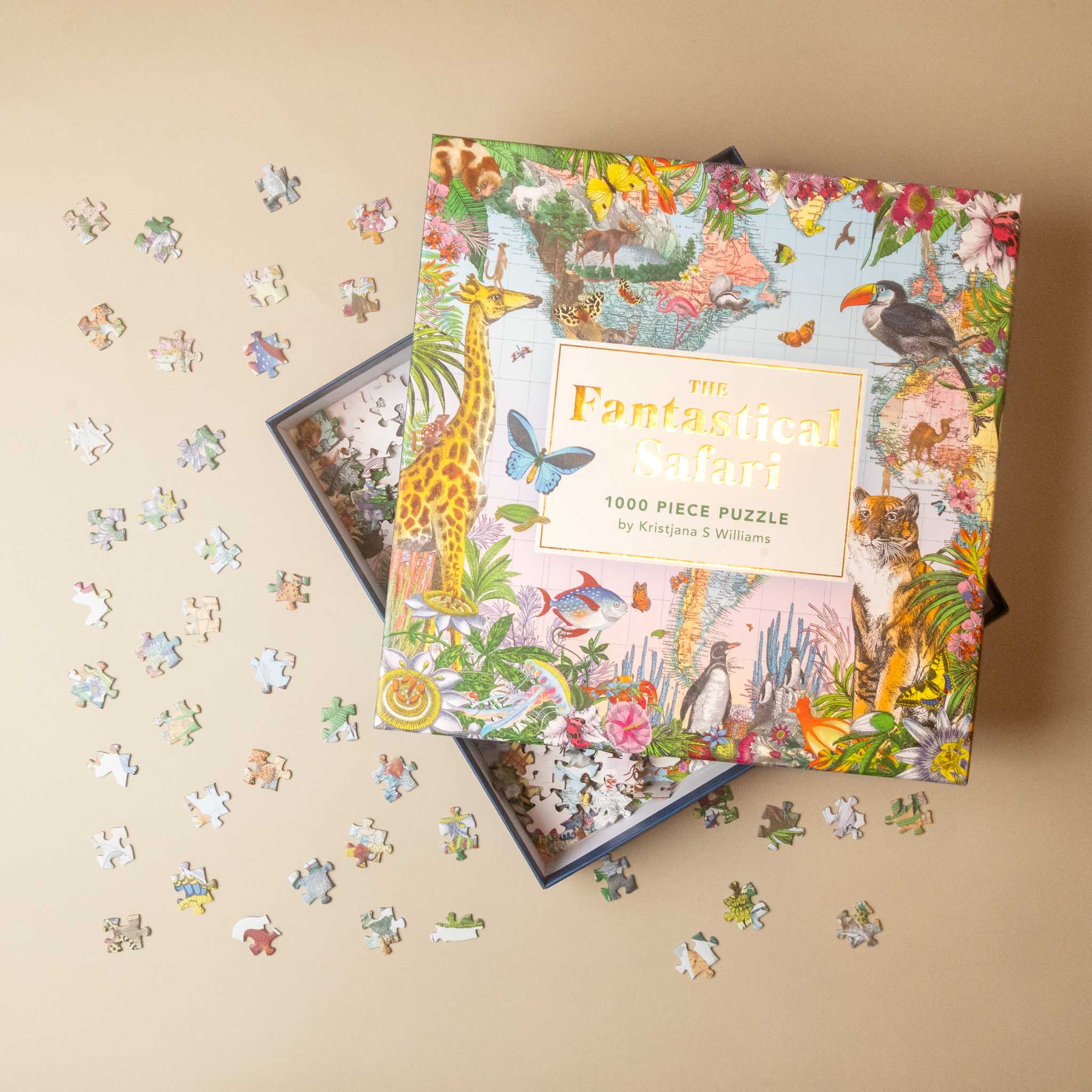 A colorful jigsaw puzzle box labeled 'The Fantastic Safari' is shown open with scattered puzzle pieces on a beige background. The box features a detailed safari illustration with animals and flowers, and the text '1000 Piece Puzzle by Kristina & Willumsen' is visible.
