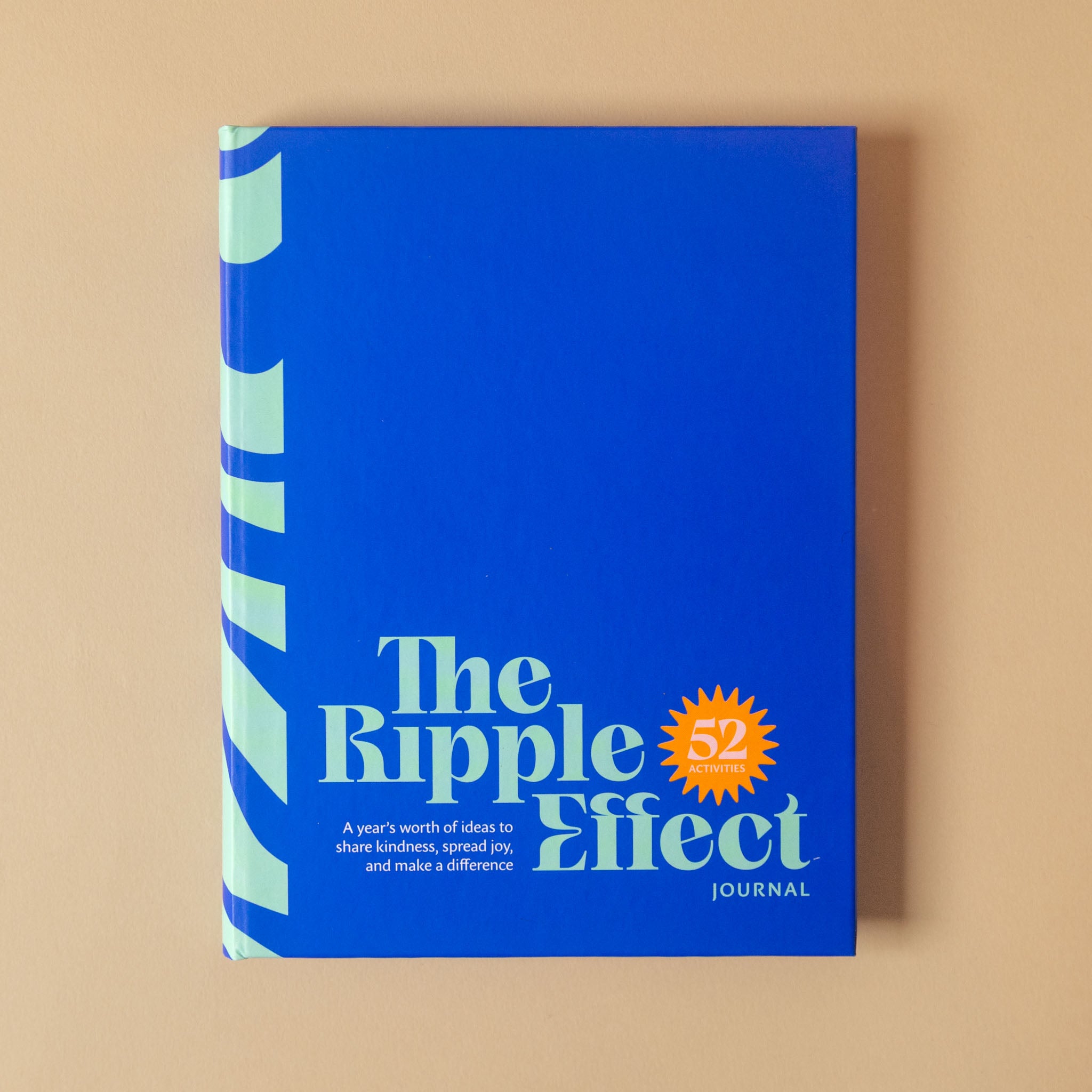 The Ripple Effect Journal, Volume 52, featuring a bright blue cover with light blue and white text and a small orange starburst accent, photographed flat on a warm beige background.