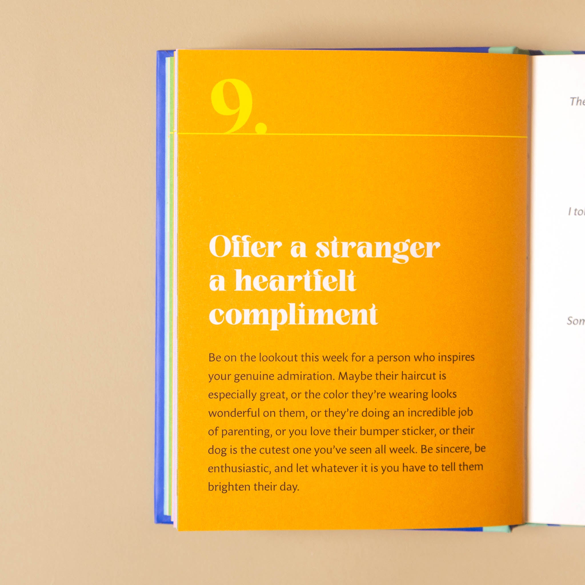 An open book or booklet showing a bright orange interior page with white text reading '9. Offer a stranger a heartfelt compliment' and a short advice paragraph, photographed against a beige background.