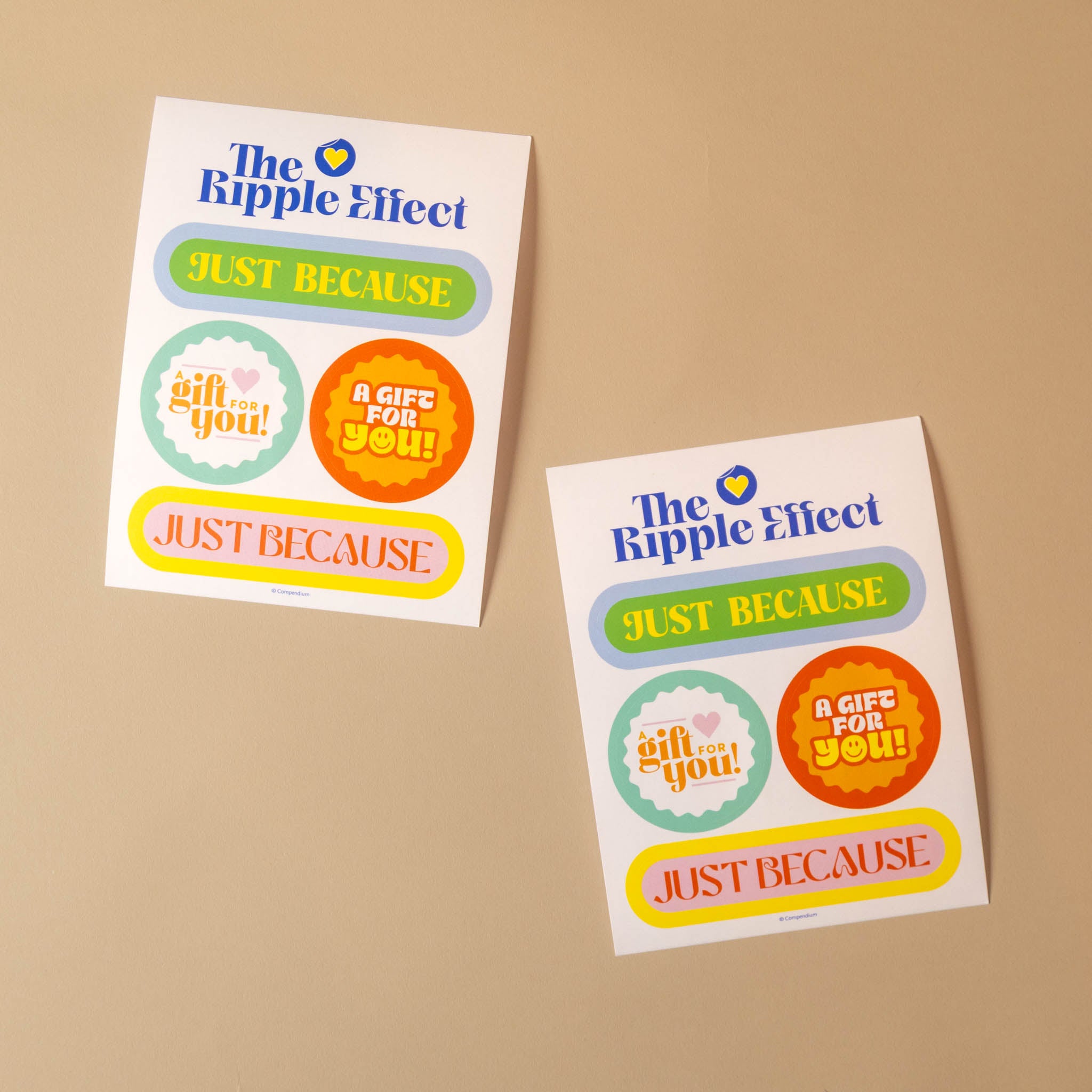 Two printed sticker sheets from The Ripple Effect on a beige background. The sheets feature colorful graphic labels including 'JUST BECAUSE' in green and yellow, circular badges reading 'gift you!' and 'A GIFT FOR YOU!', and a small blue heart icon.