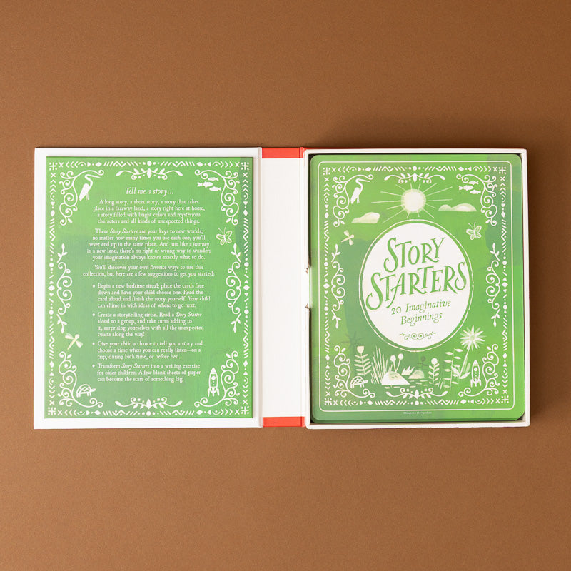 An open deck of cards titled 'Story Starters' laid flat on a brown background. The cards have a light green and white illustrated design with decorative borders and text, and a red-orange edge visible along the spine area.