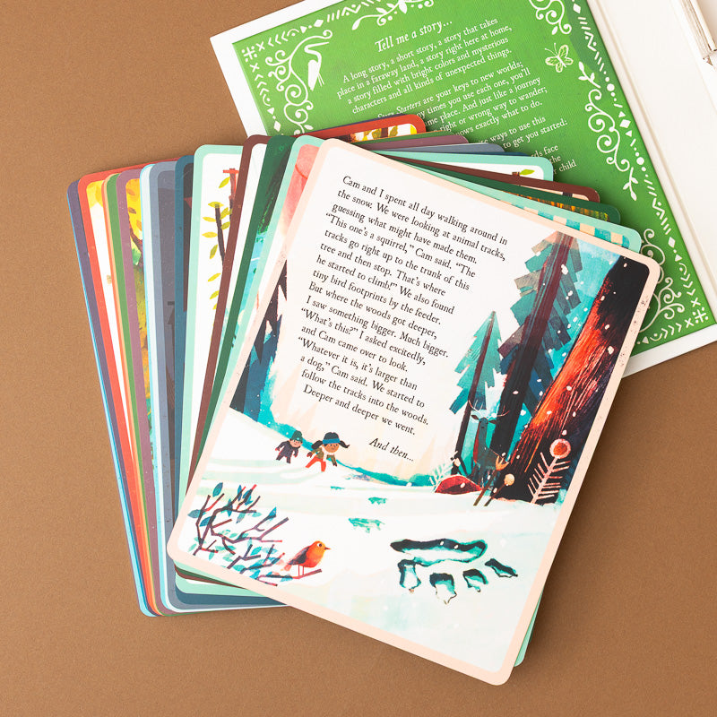 A fanned-out children's picture book or card storybook set on a tan surface, showing illustrated cards with a winter forest scene on the top card and a green title page behind it.