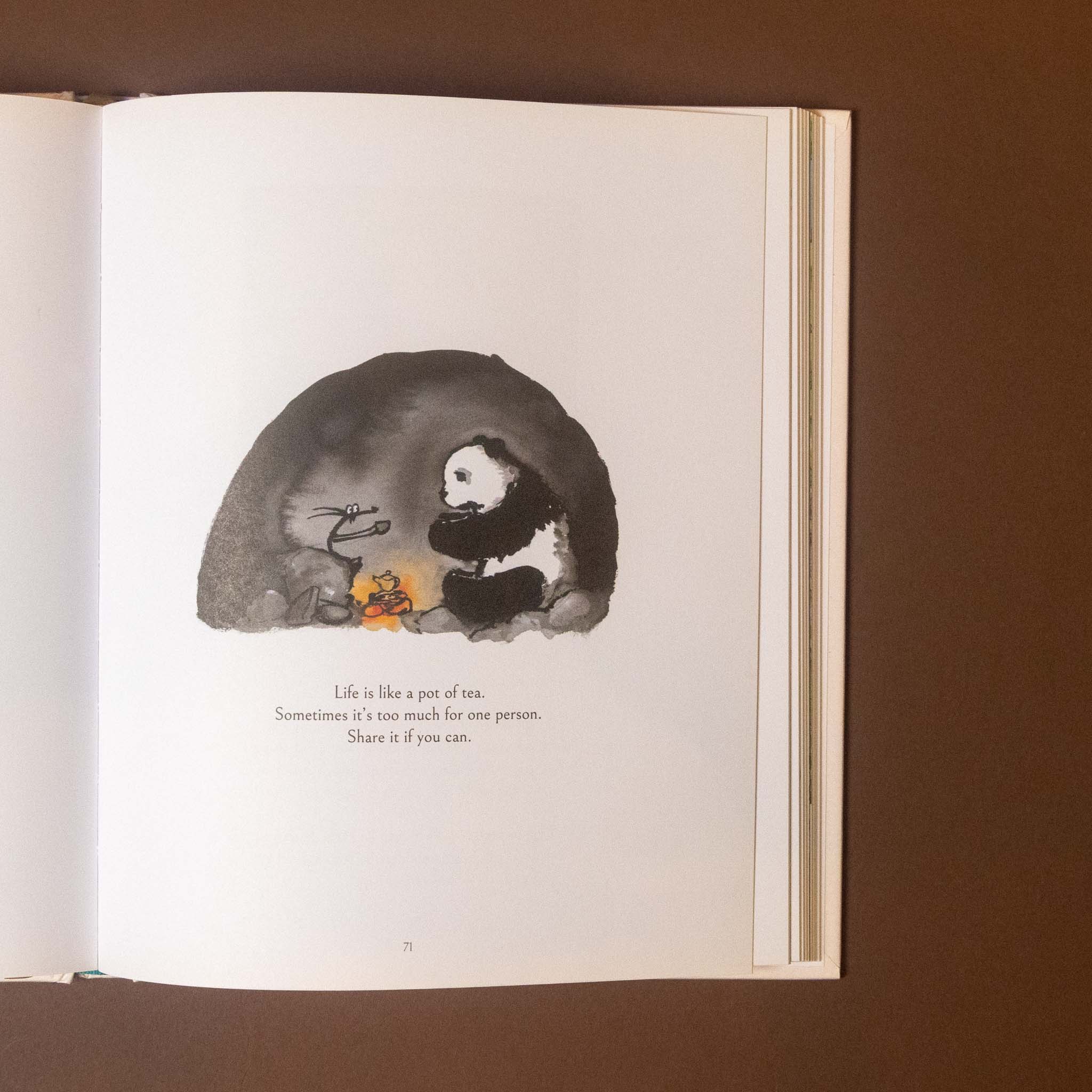 An open book lying on a brown surface, showing a printed page with a black-and-white illustration of a panda under a cave-like shape and a short quote below.