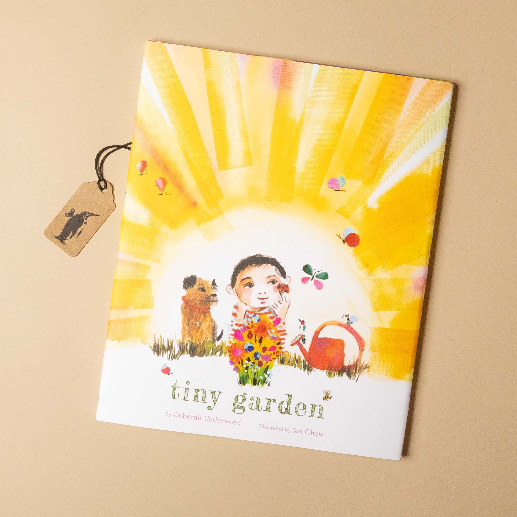 Book titled 'tiny garden' with a colorful cover featuring a child and dog under a sun, on a beige background.