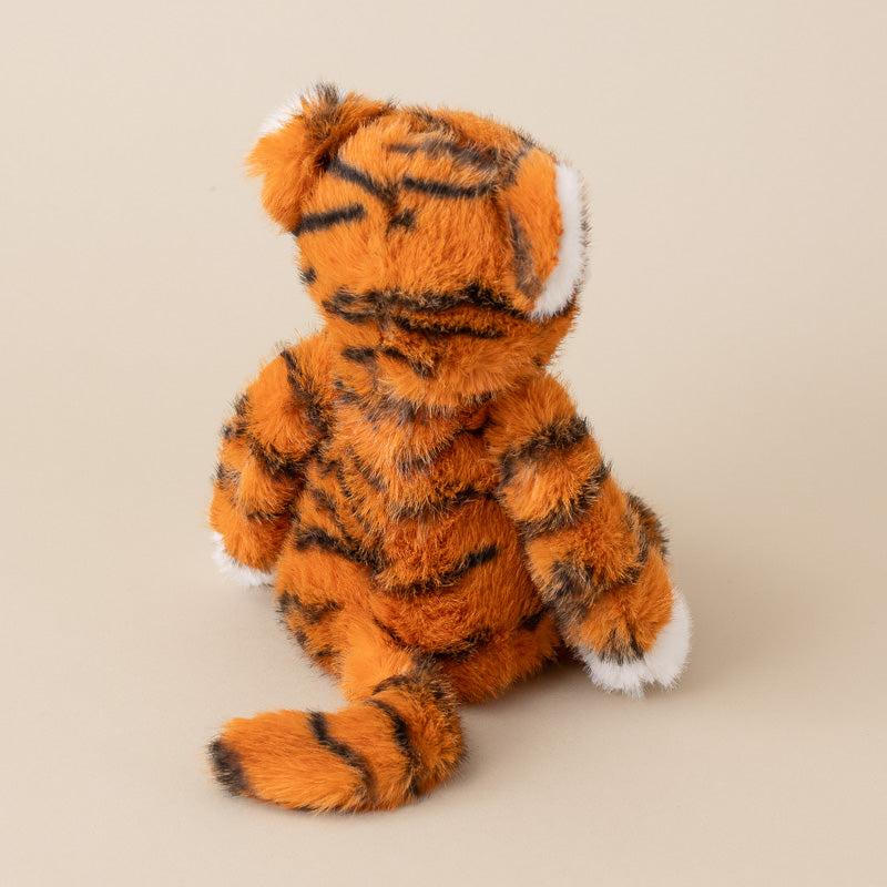 A plush tiger toy shown from the back, featuring orange fur with black stripes and white accents on its paws, feet, and ears, set against a solid beige background.