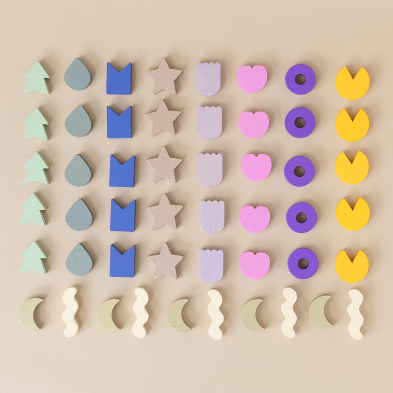 A set of pastel-colored wooden shape cutouts arranged in rows on a beige background. The shapes include trees, raindrops, crowns, stars, tulips, hearts, donuts, and crescent moons in mint green, blue, beige, lavender, pink, purple, and yellow.