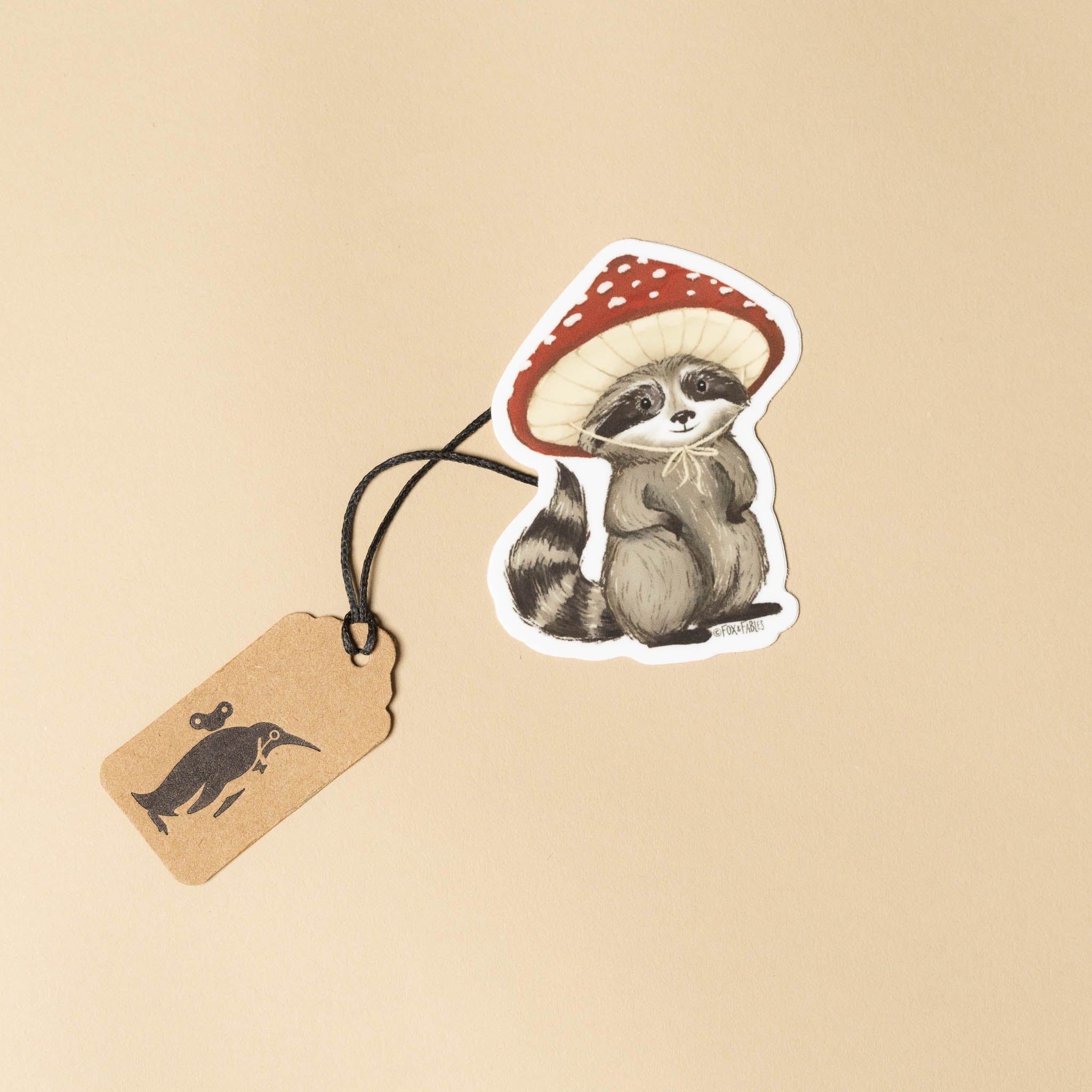 Sticker of a raccoon wearing a mushroom hat with a tag on a beige background
