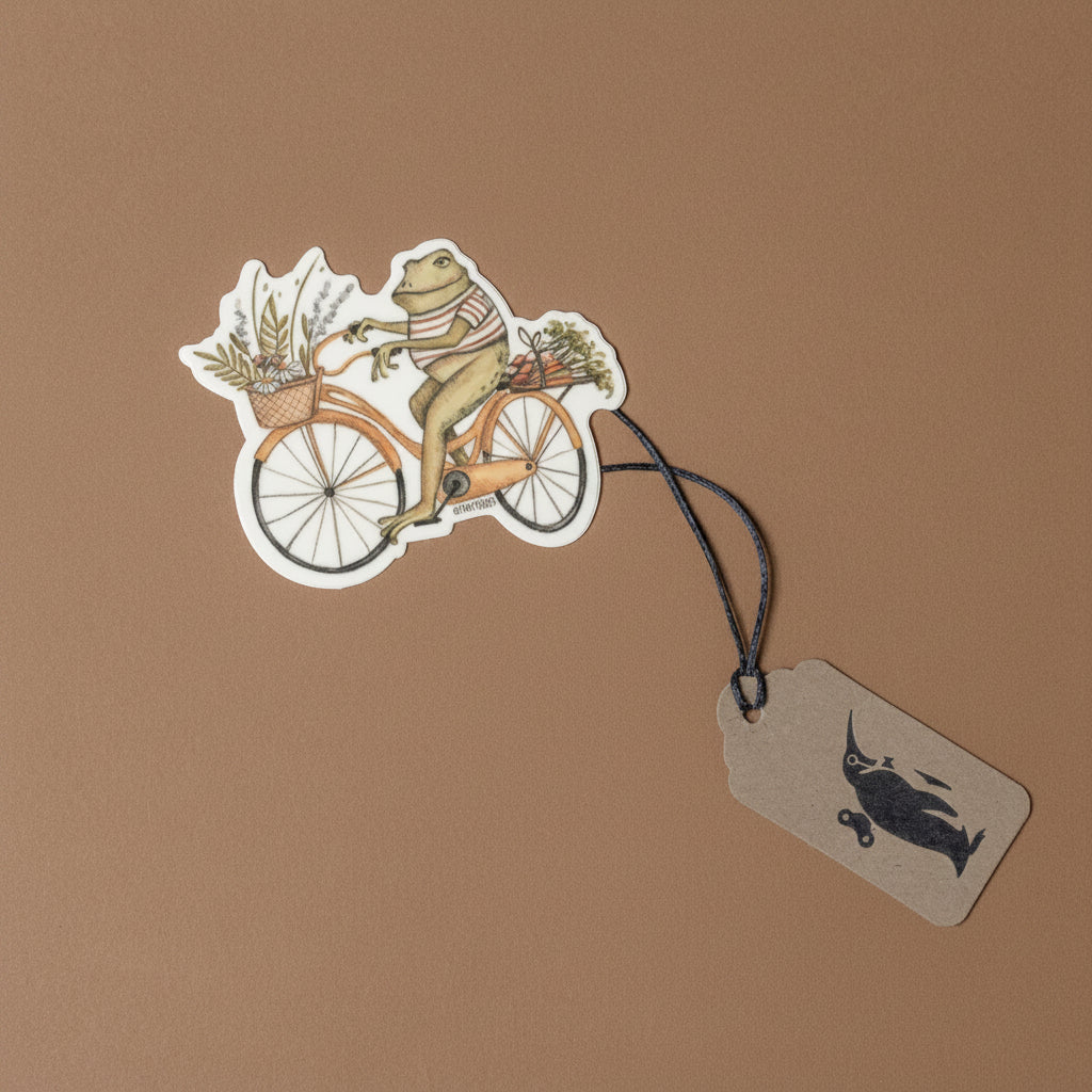 Frog on a bicycle with a basket, attached to a tag on a brown background