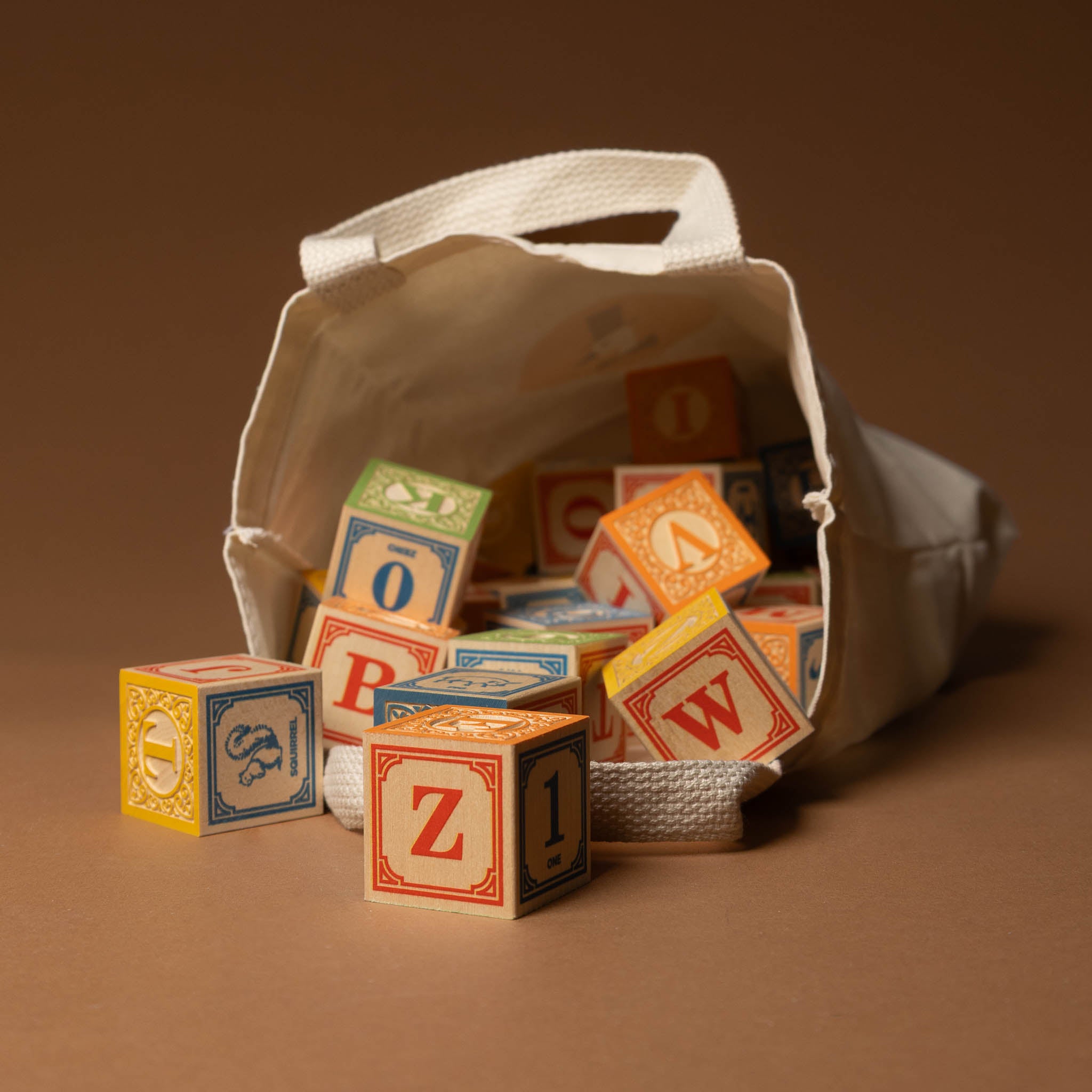 wooden-block-set-with-canvas-bag-classic-abcs Colorful alphabet blocks spilling out of a white bag on a brown background