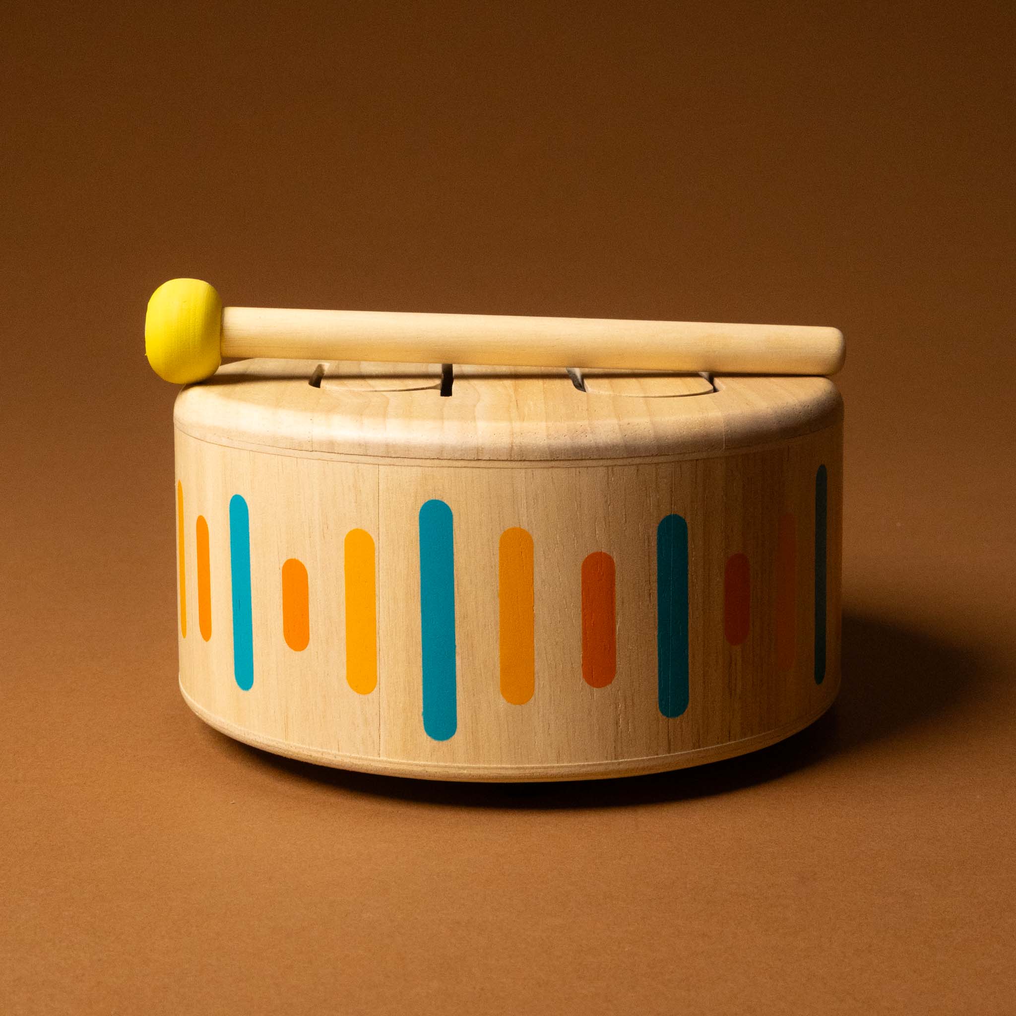 Wooden toy drum with colorful patterns and a drumstick on a brown background