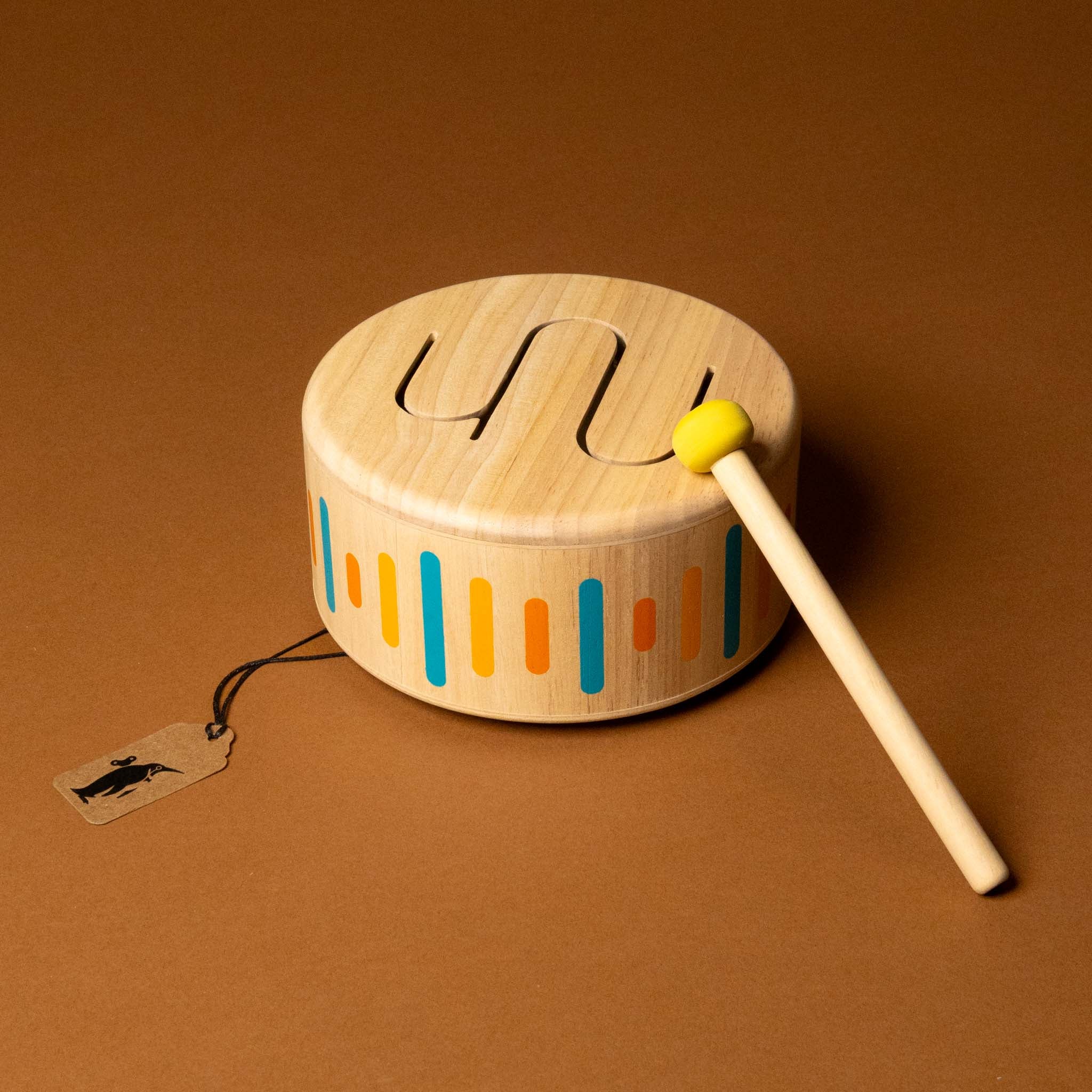 Wooden toy drum with colorful patterns and a drumstick on a brown background