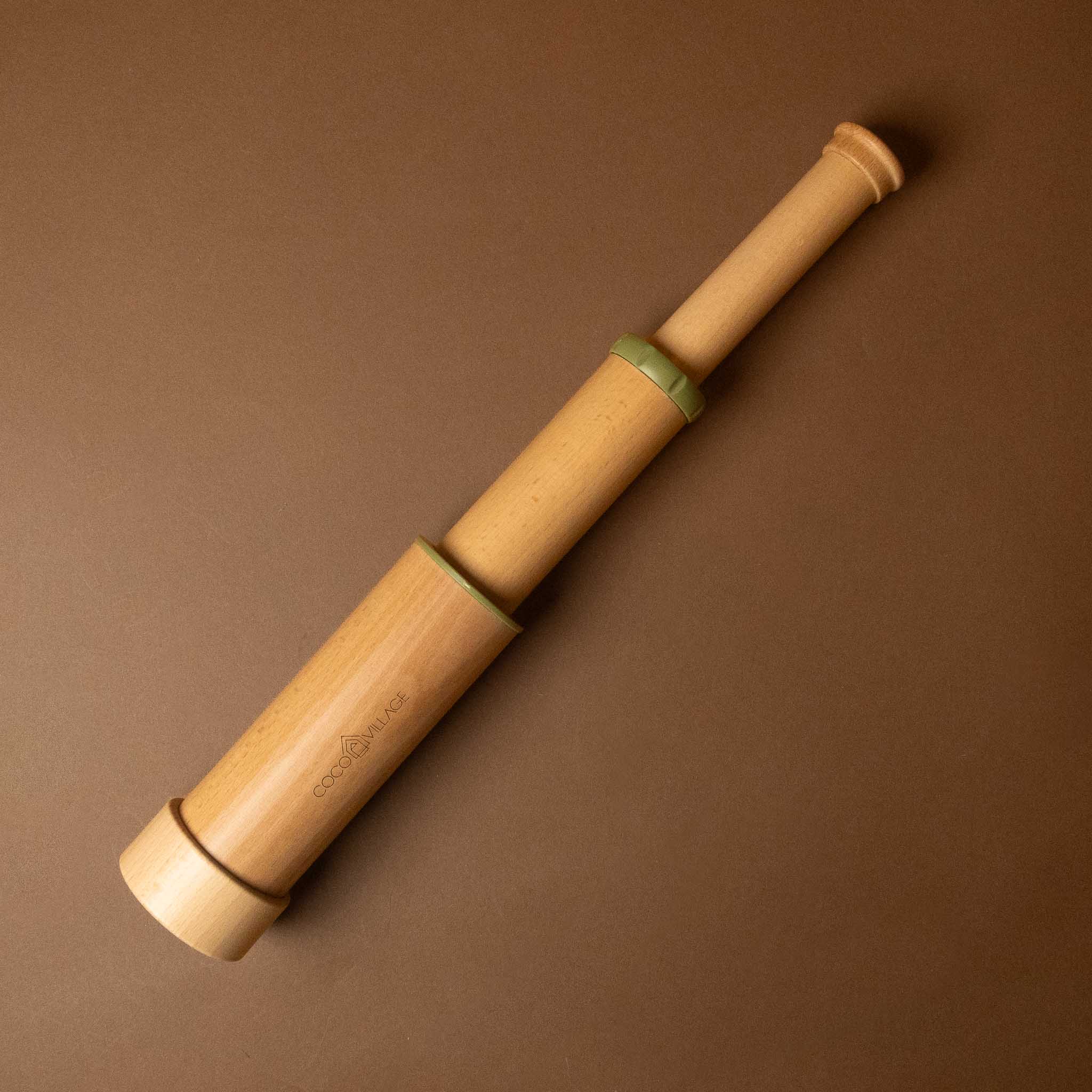 A light natural wood toy telescope with green plastic rings, shown on a solid brown background.