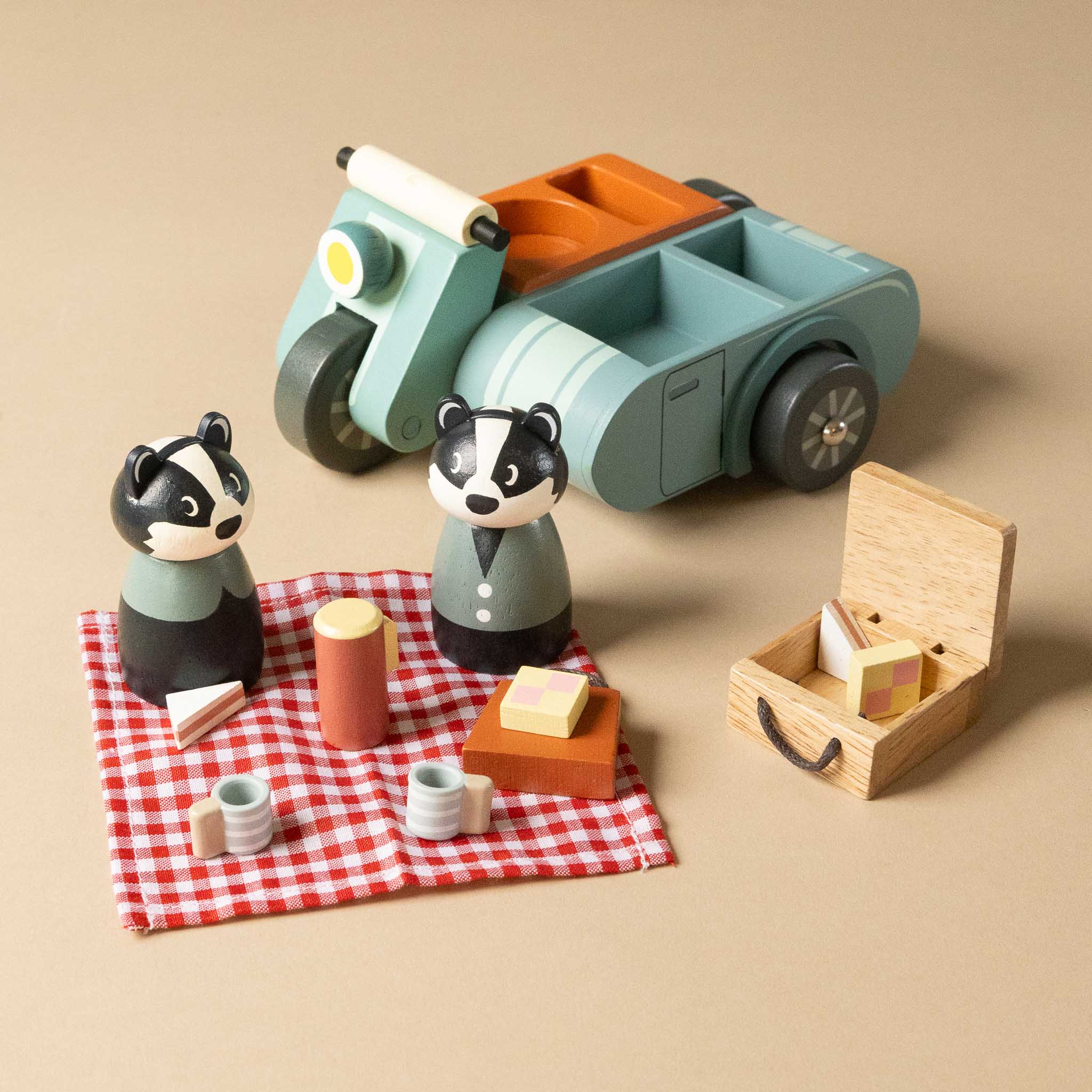 wooden-motorbike-picnic-play-set with two badger figures and a picnic setup on a beige background