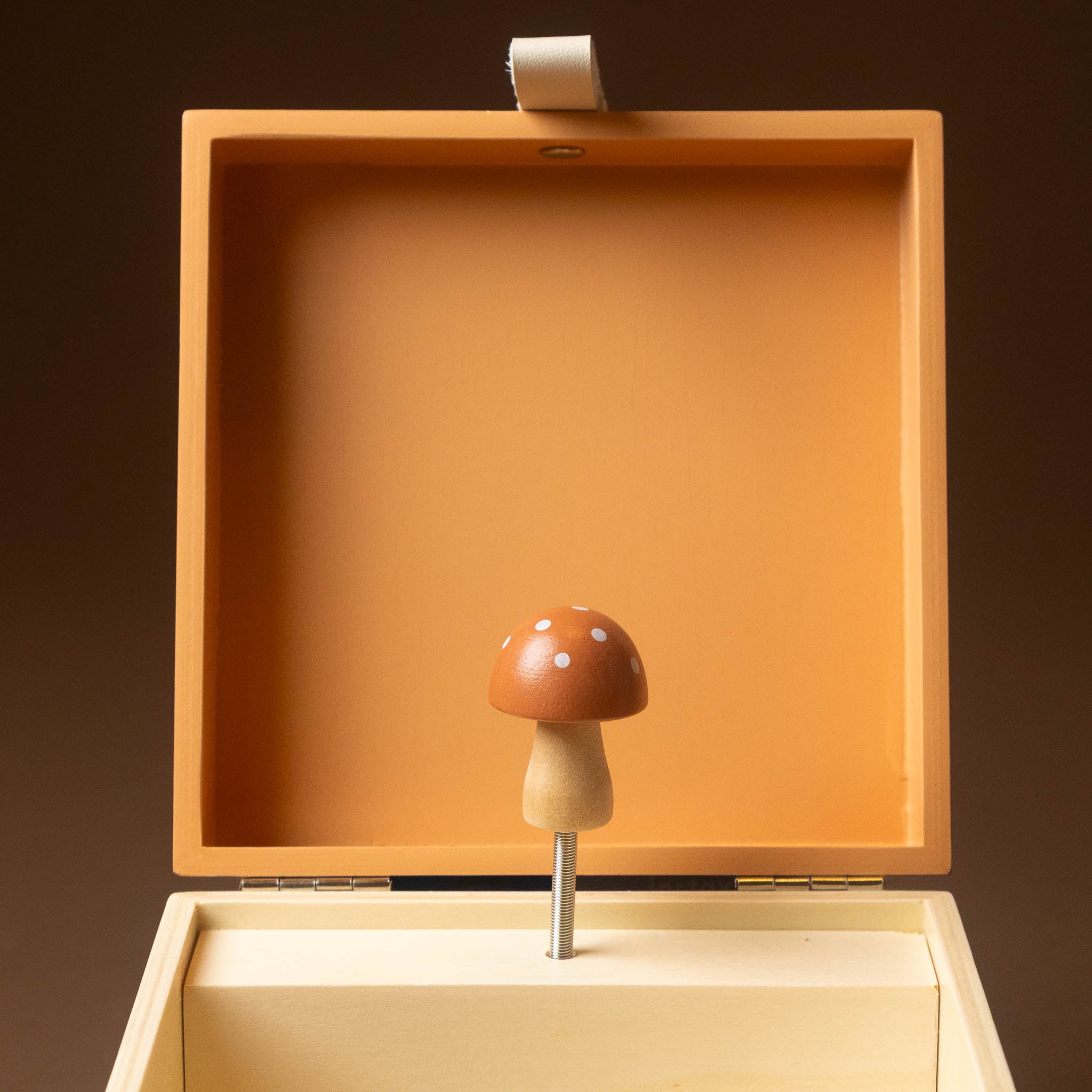 wooden-musical-treasures-box-nature wooden mushroom-shaped music box with an open peach-colored lid and cream-colored base, set against a dark brown background.