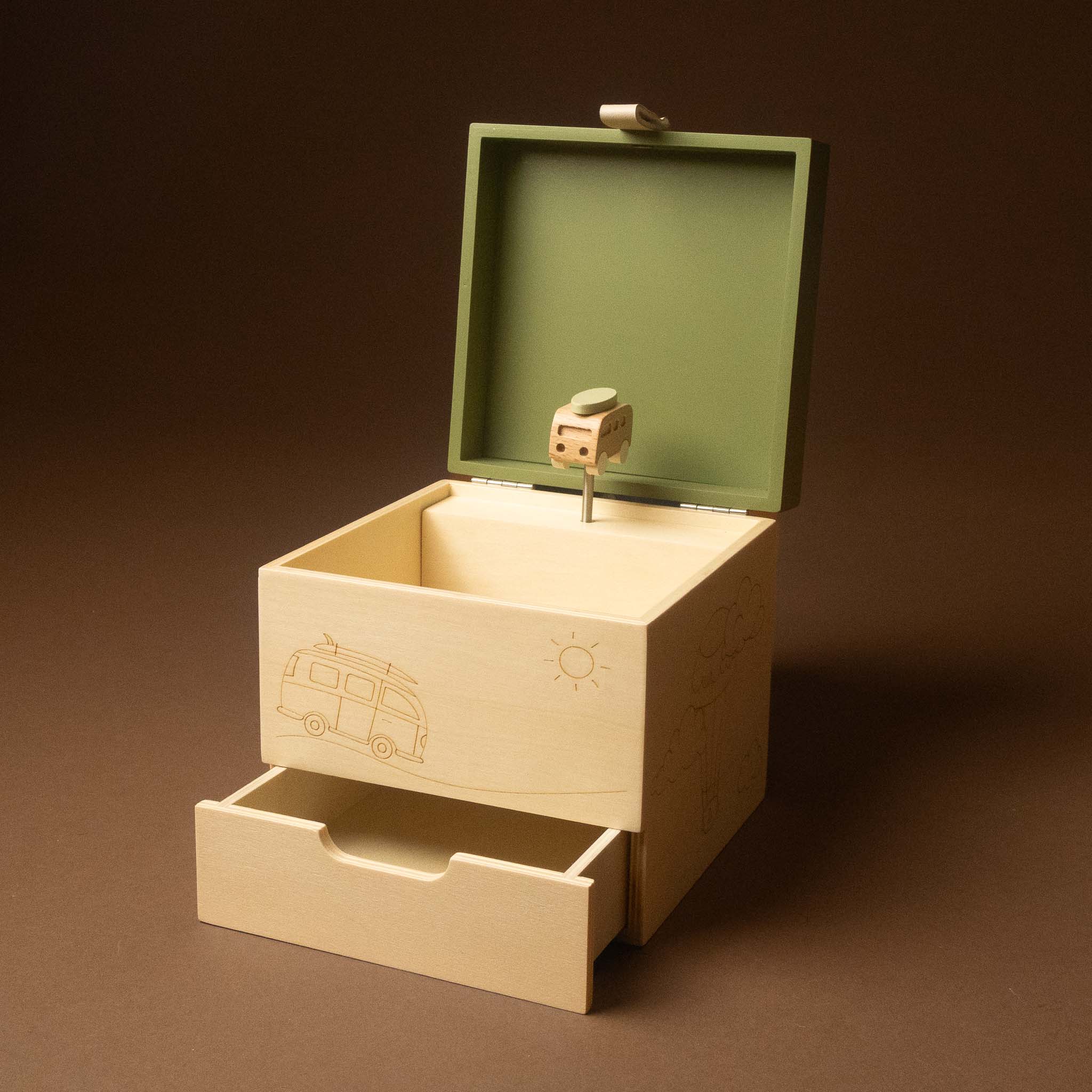 wooden-musical-treasures-box-road-warrier with an open lid and a single drawer, shown on a dark brown studio background. The box is made of light natural wood with engraved illustrations of a camper van and a sun, and has a small toy figure on a pin inside the open lid.
